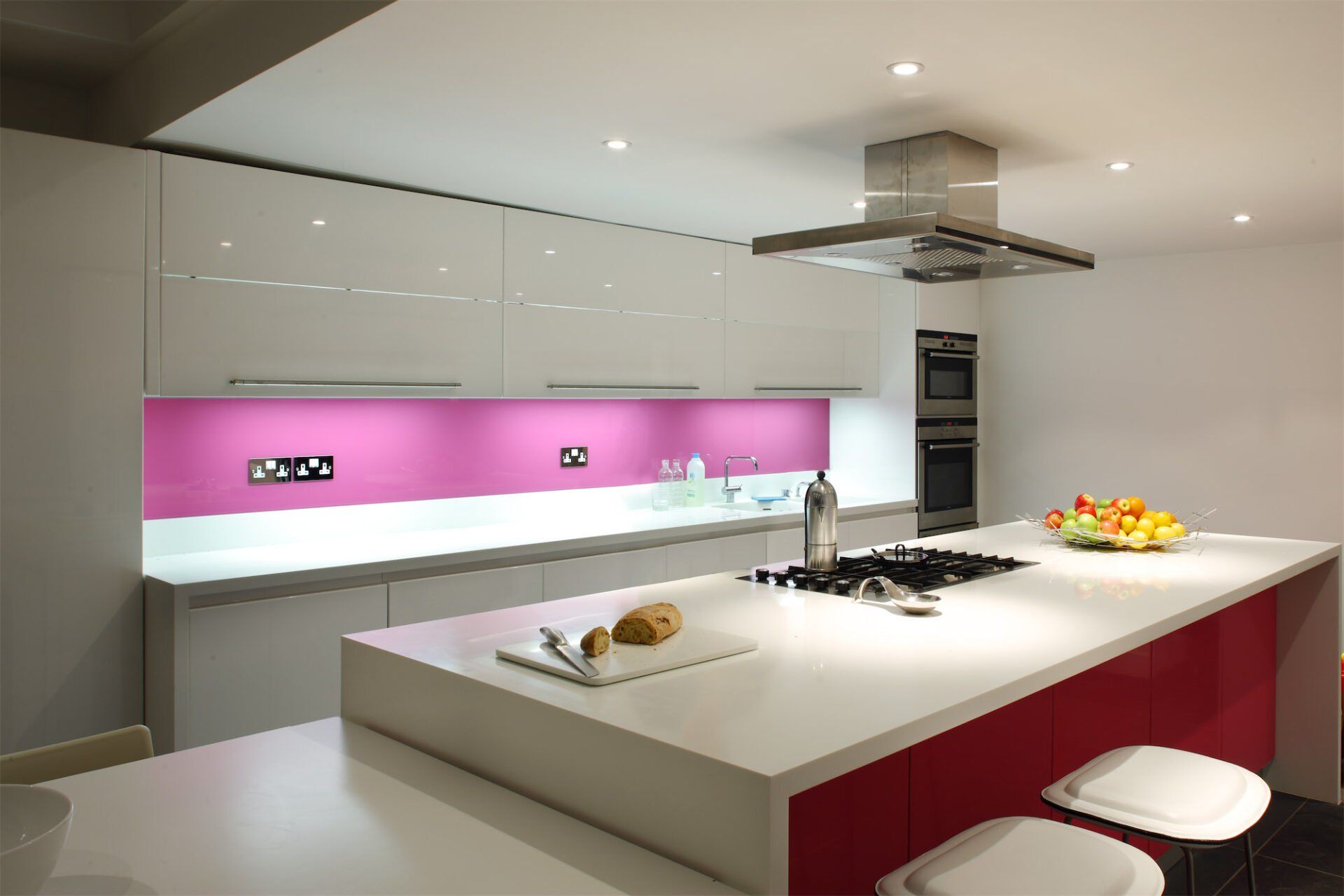 Modern kitchen with white cabinets, magenta backsplash, and red island.