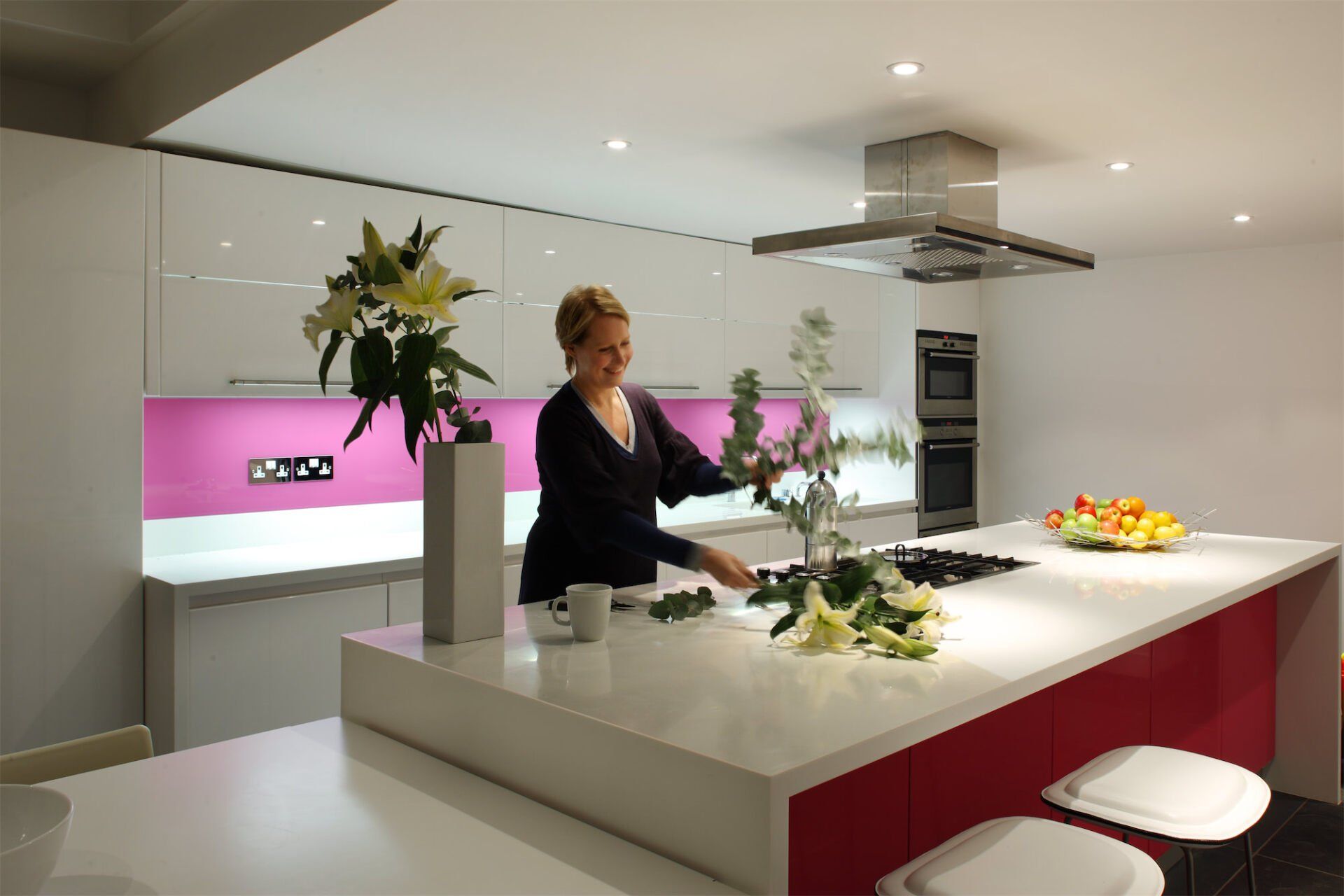 Woman arranging flowers in a modern white and red kitchen.
