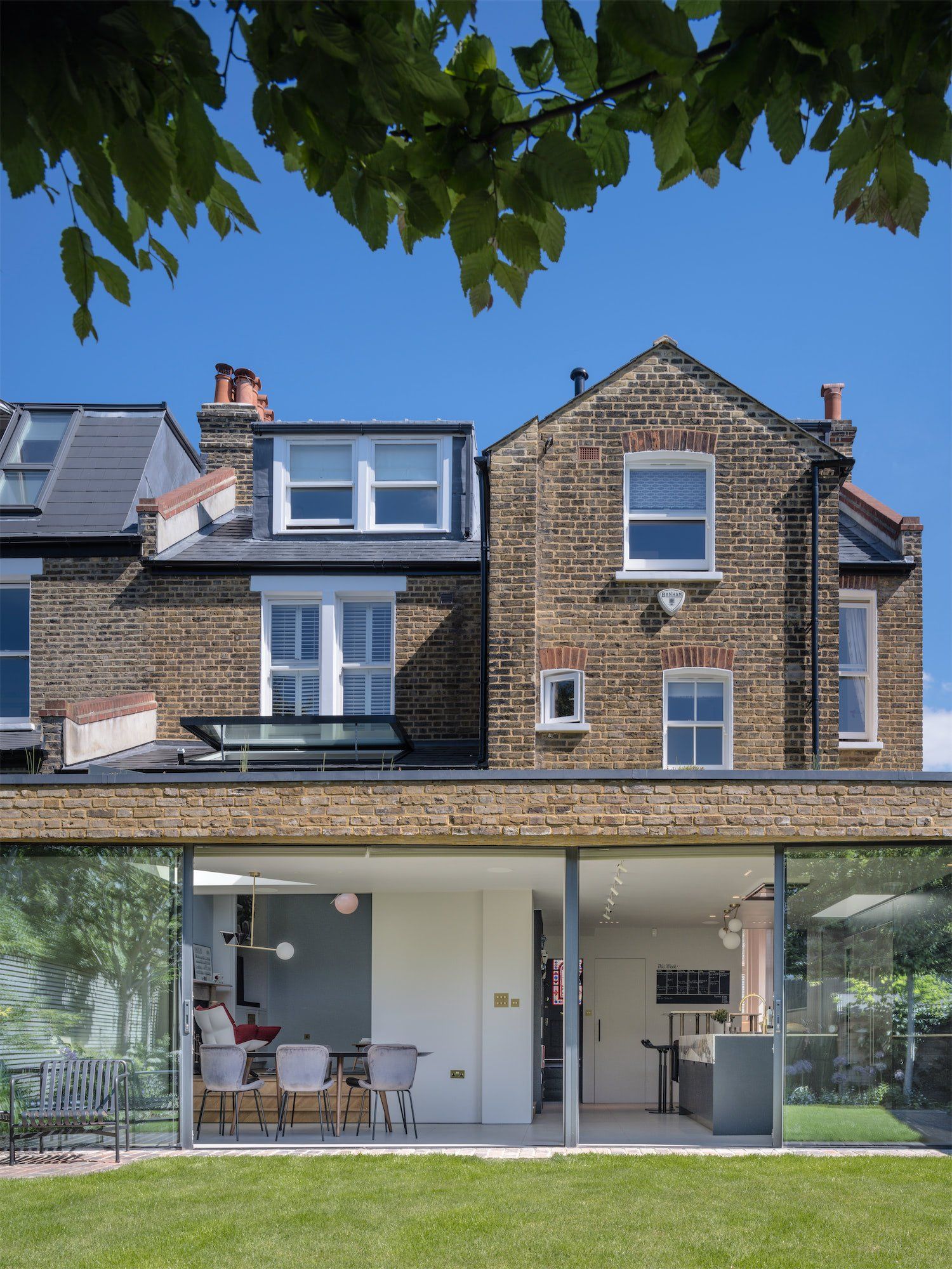 Modern brick house with glass ground floor and leafy branches overhead
