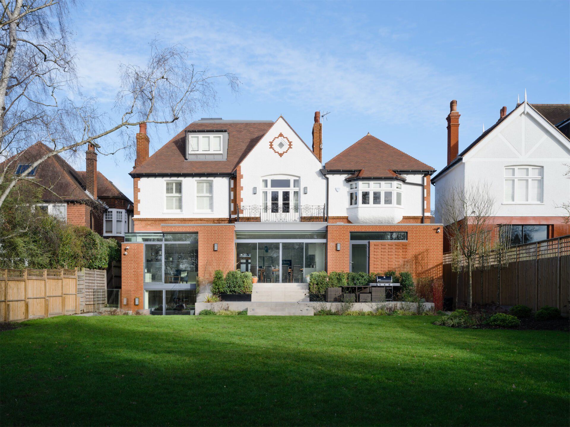 Large white house with red roofs and a green backyard under a clear blue sky