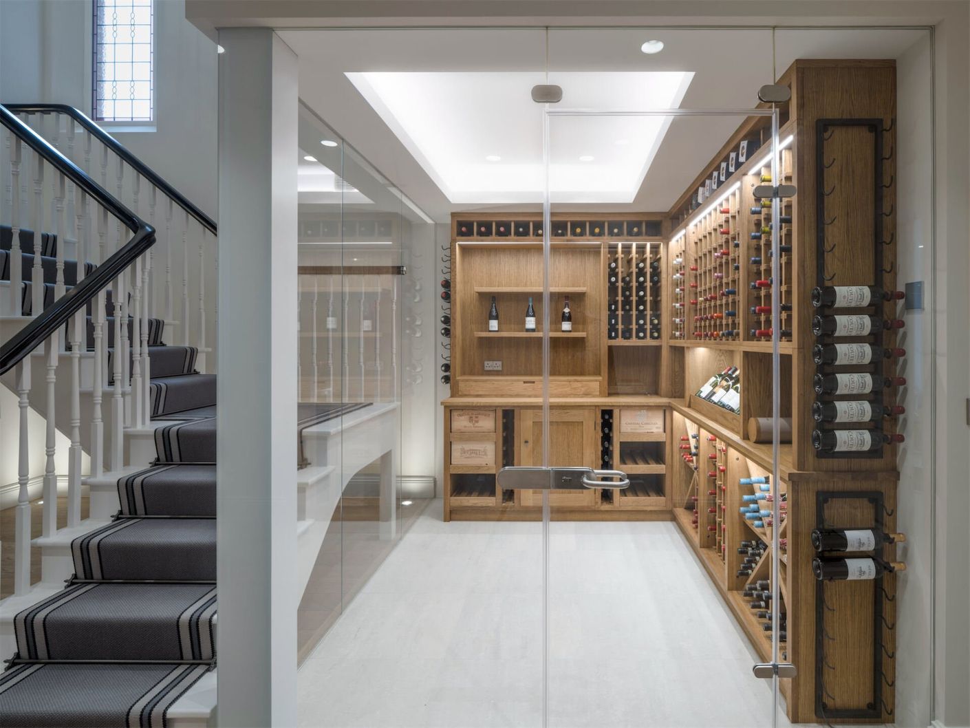 Bright home wine cellar with wooden racks, glass doors, and a staircase beside it