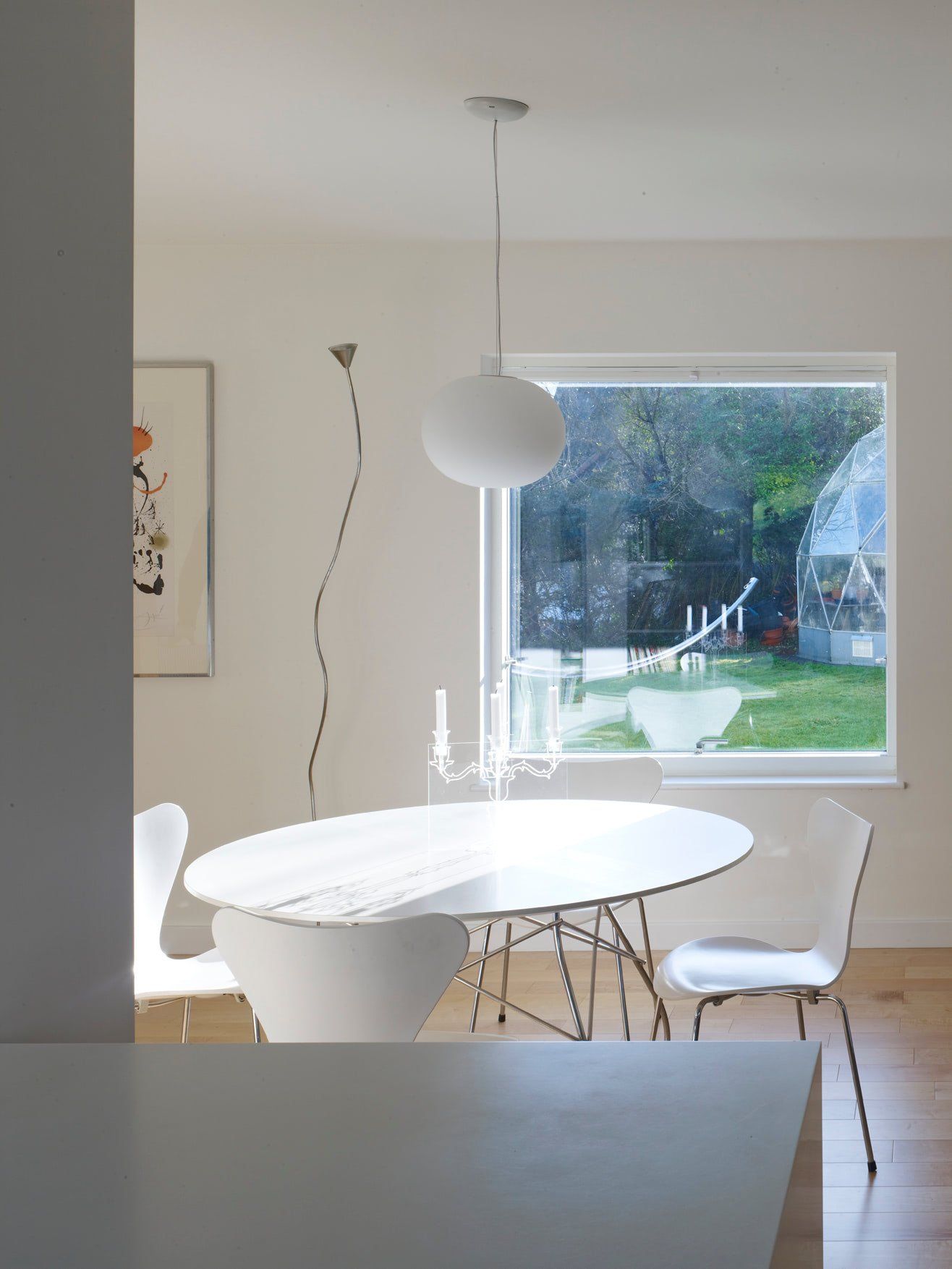 Modern dining room with white round table, chairs, pendant light, and large window overlooking a backyard.