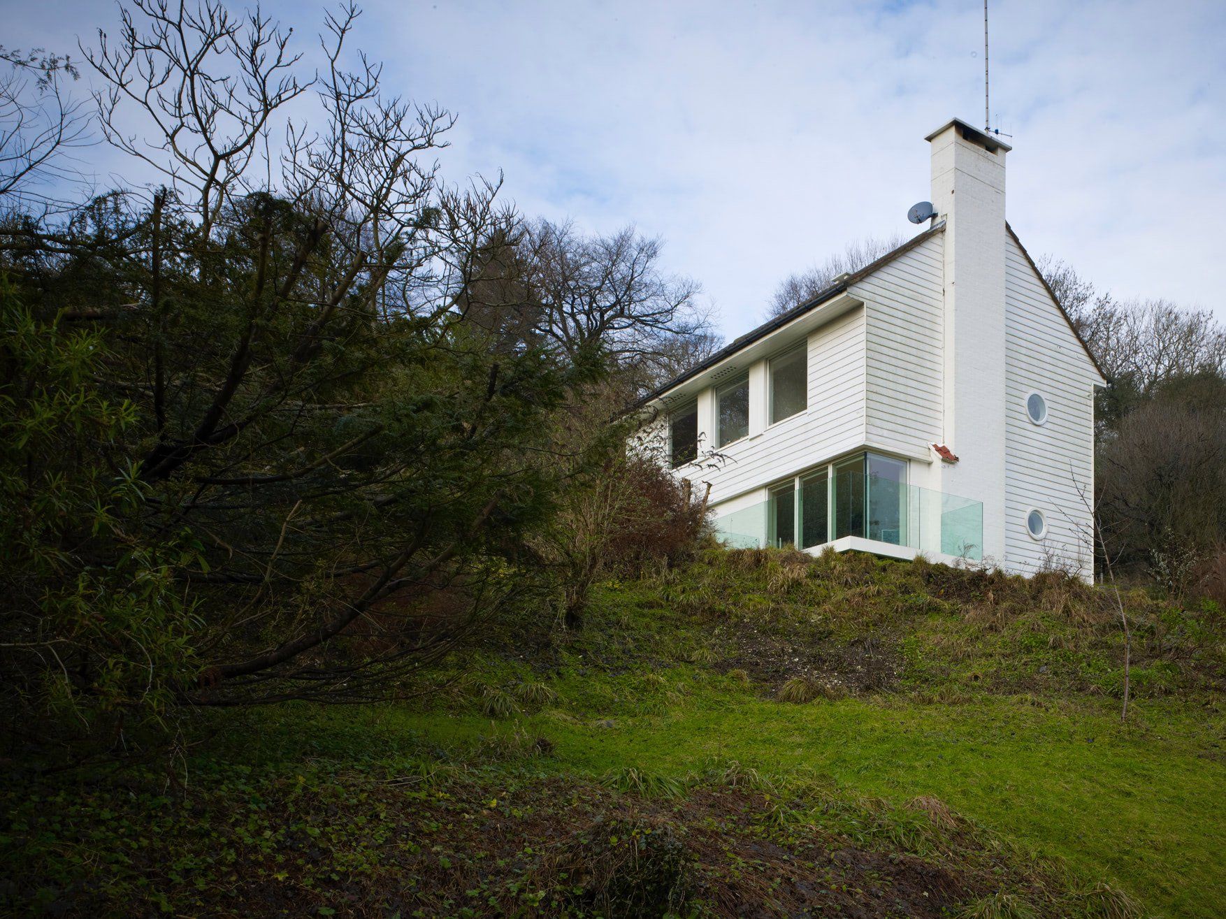 White house on a grassy hillside with bare trees under an overcast sky