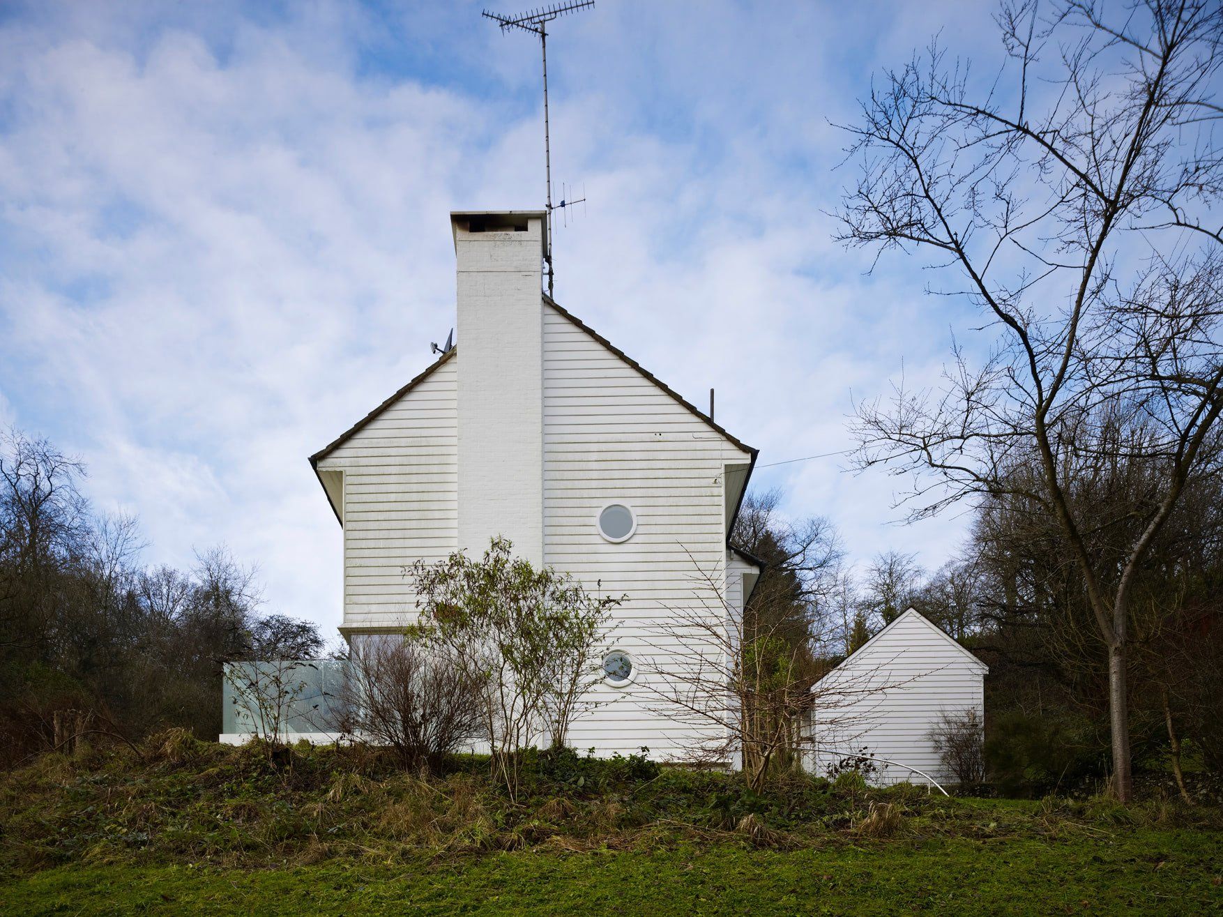 White house-like building with a chimney on a grassy hill under a cloudy sky