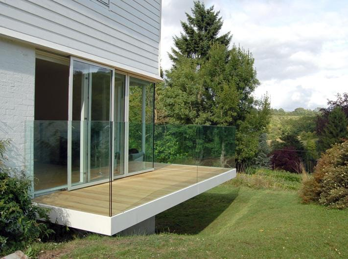 Modern house deck with glass railing and wooden floor overlooking a grassy yard