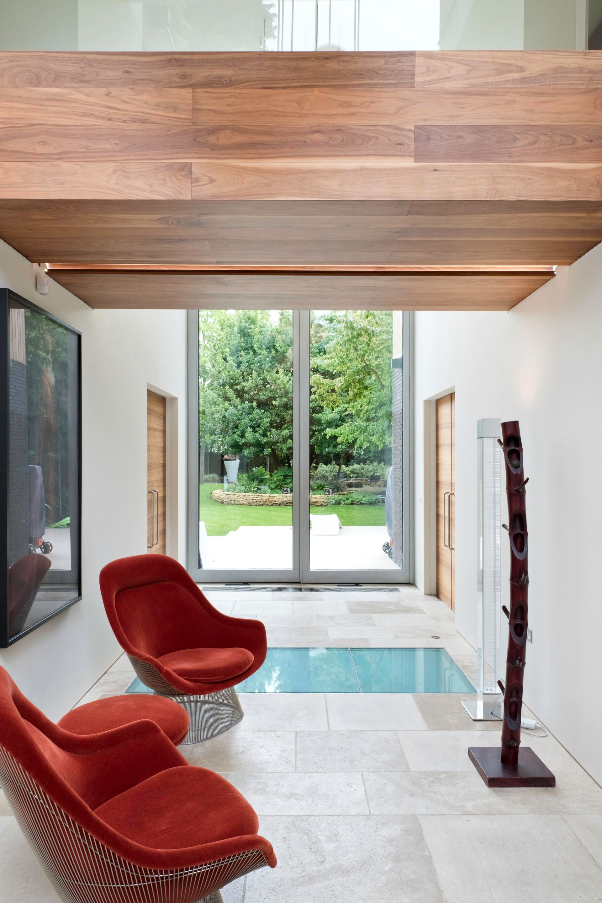 Modern living room with wood ceiling, red chairs, glass doors, and a pool view outside