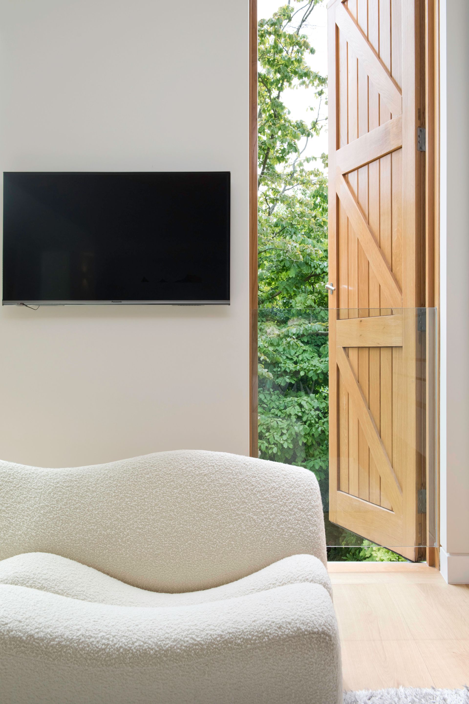 Minimal living room with wall-mounted TV, white sofa, and open wooden door to greenery