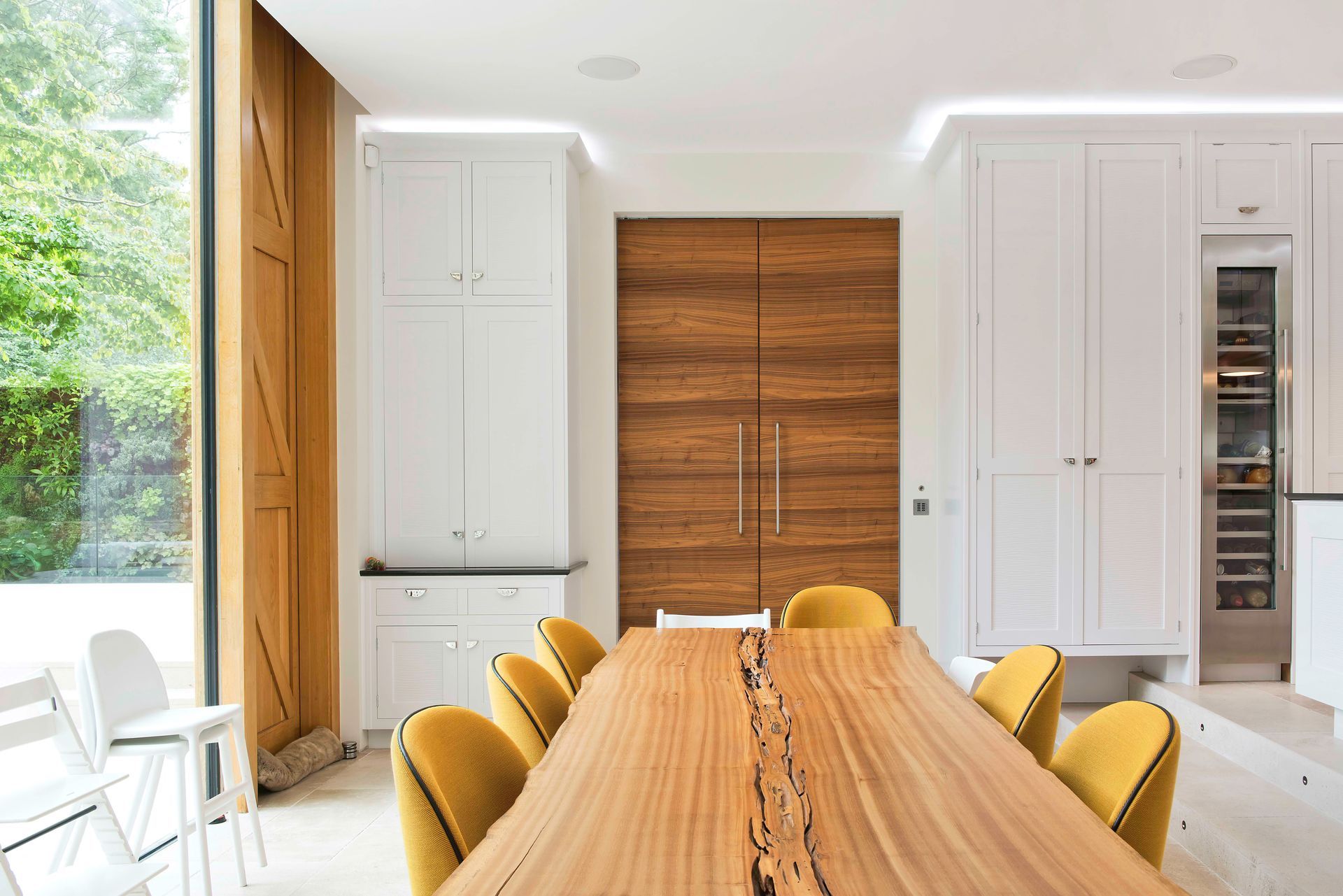 Bright modern dining room with a long wooden table, yellow chairs, and large windows.