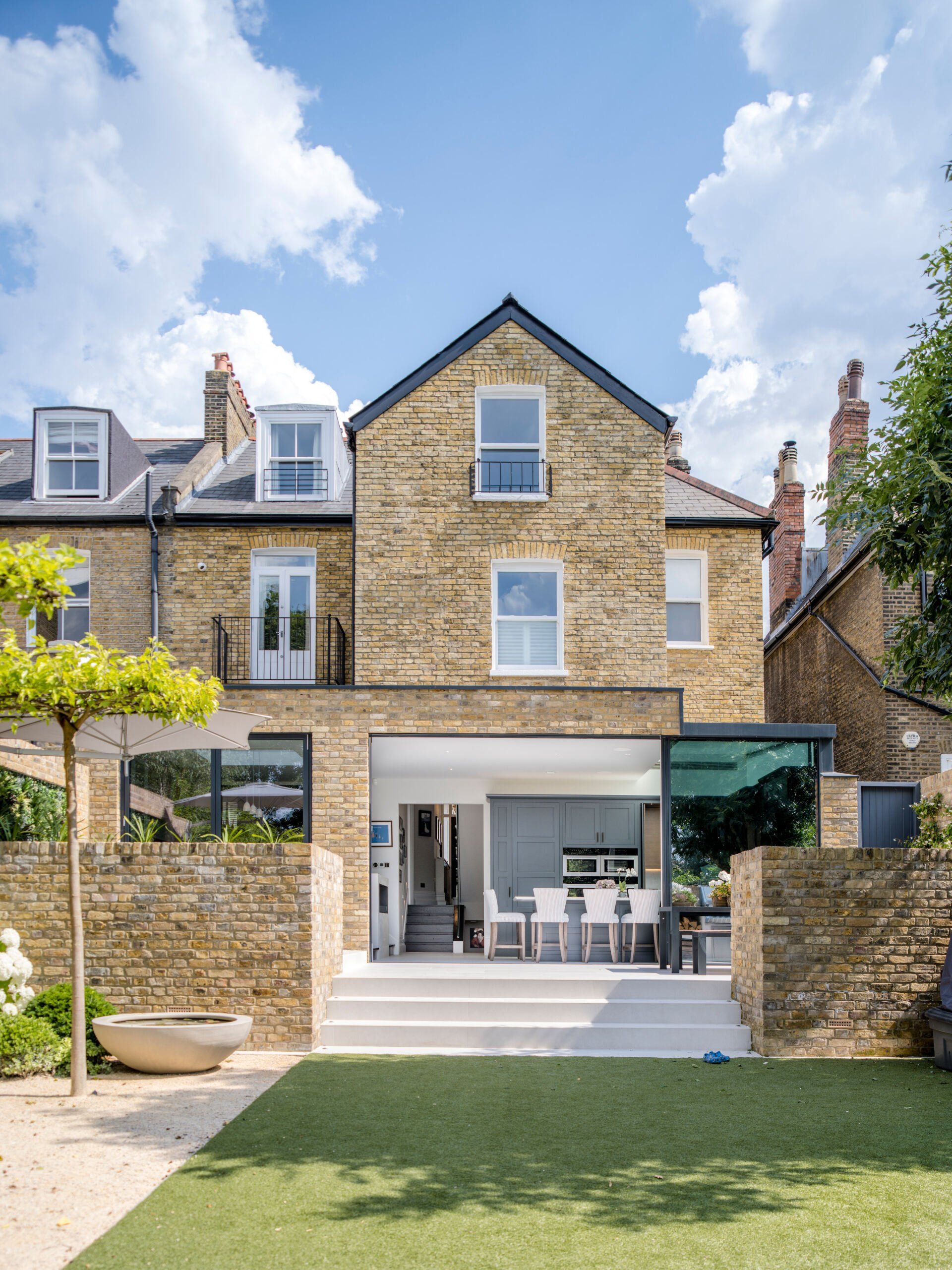 Stone townhouse with a patio and lawn, featuring an open ground-floor dining area under a blue sky.