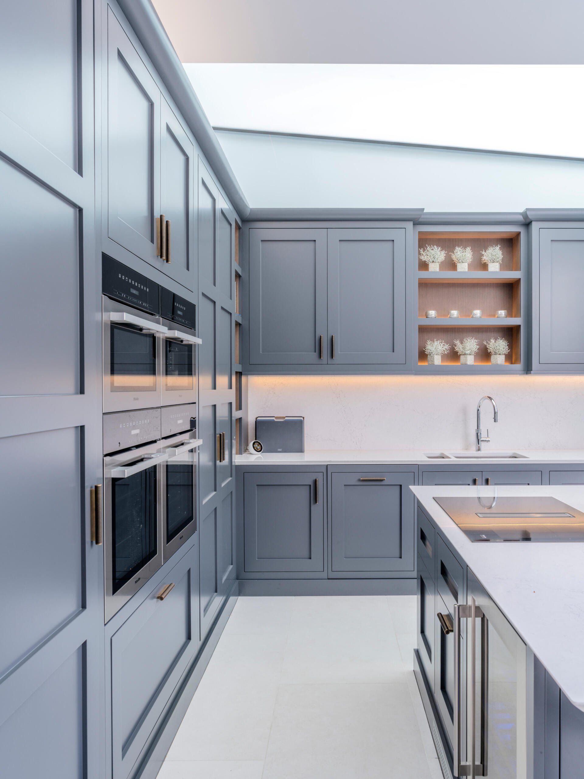 Modern gray kitchen with built-in appliances, white countertops, and glass-front cabinets displaying dishes
