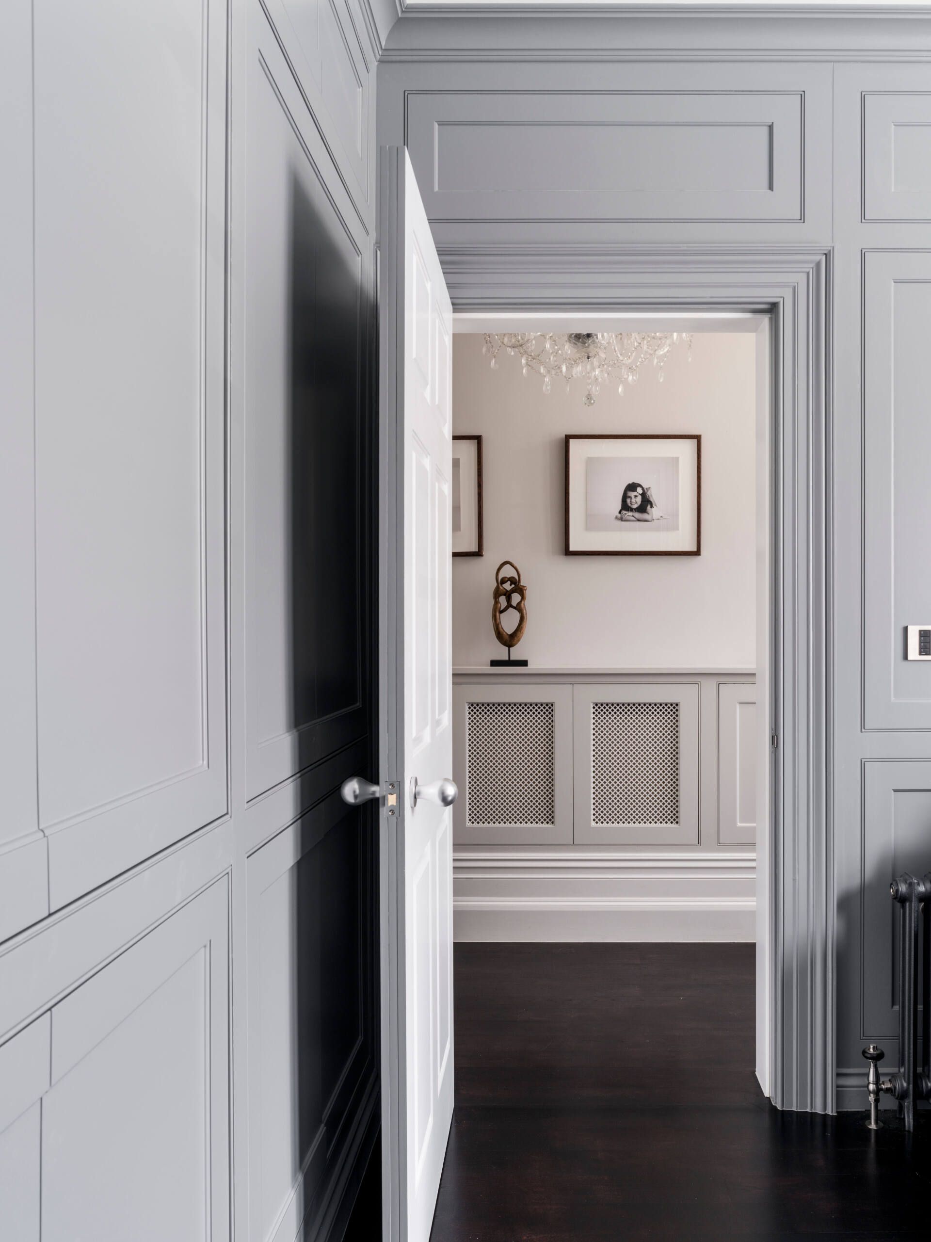 Open doorway to a bright, elegant room with framed art, white wainscoting, and dark wood floors.
