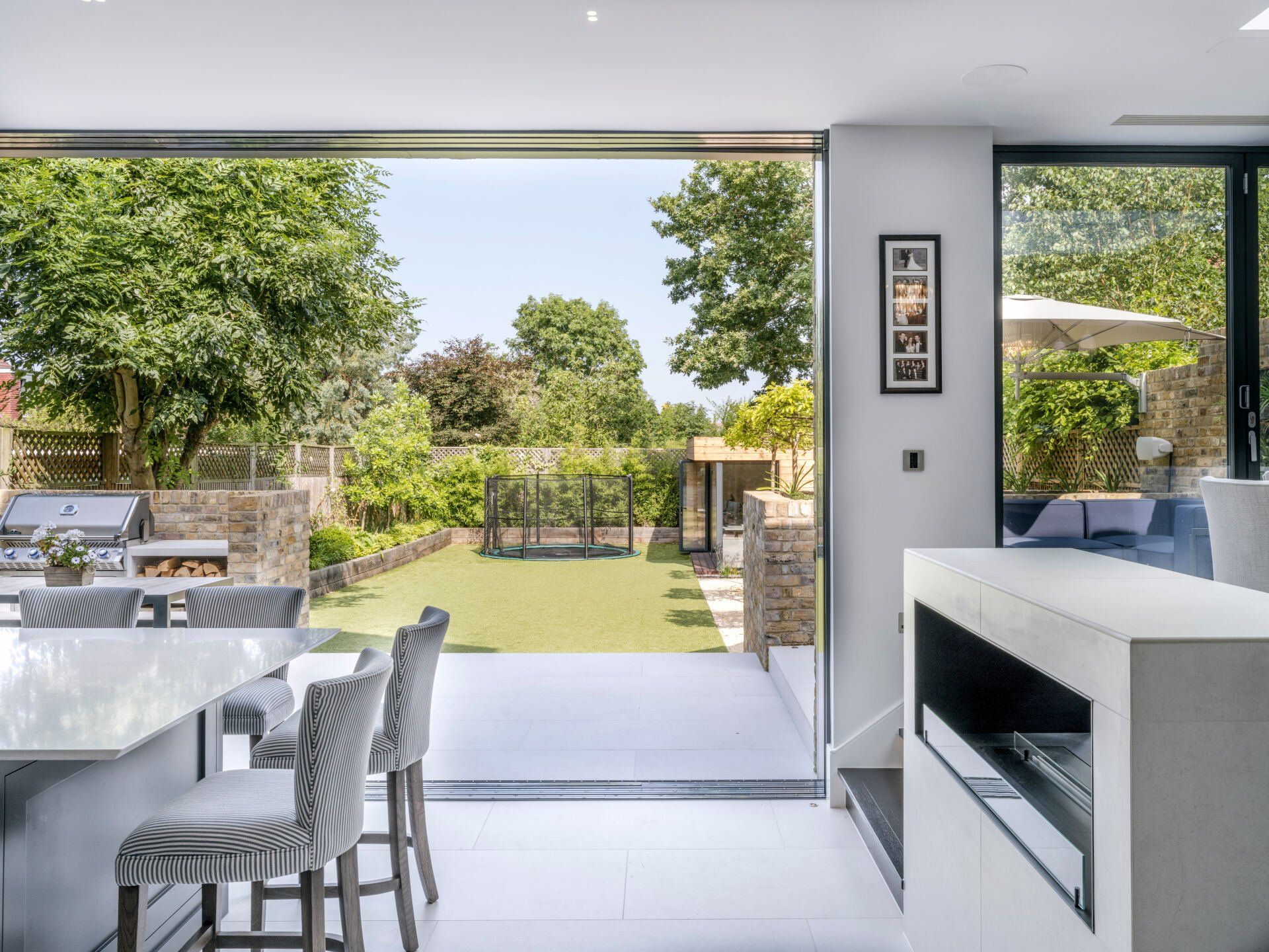Modern patio dining area opening to a green garden with sliding glass doors and outdoor seating