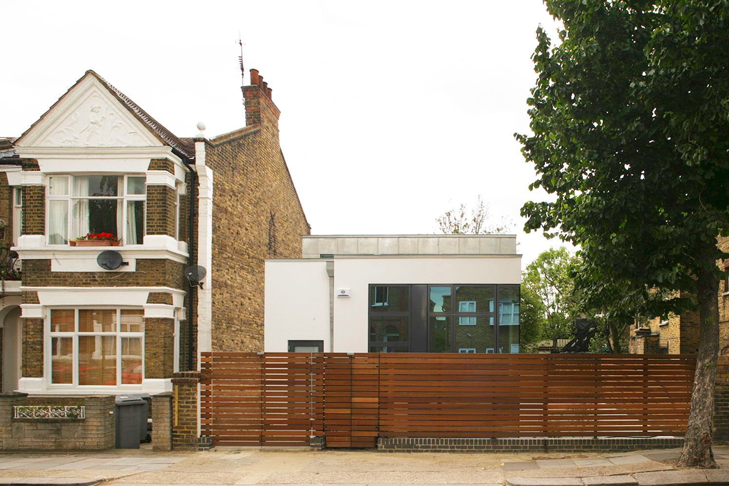 Traditional house beside a modern white building behind a wooden fence and trees