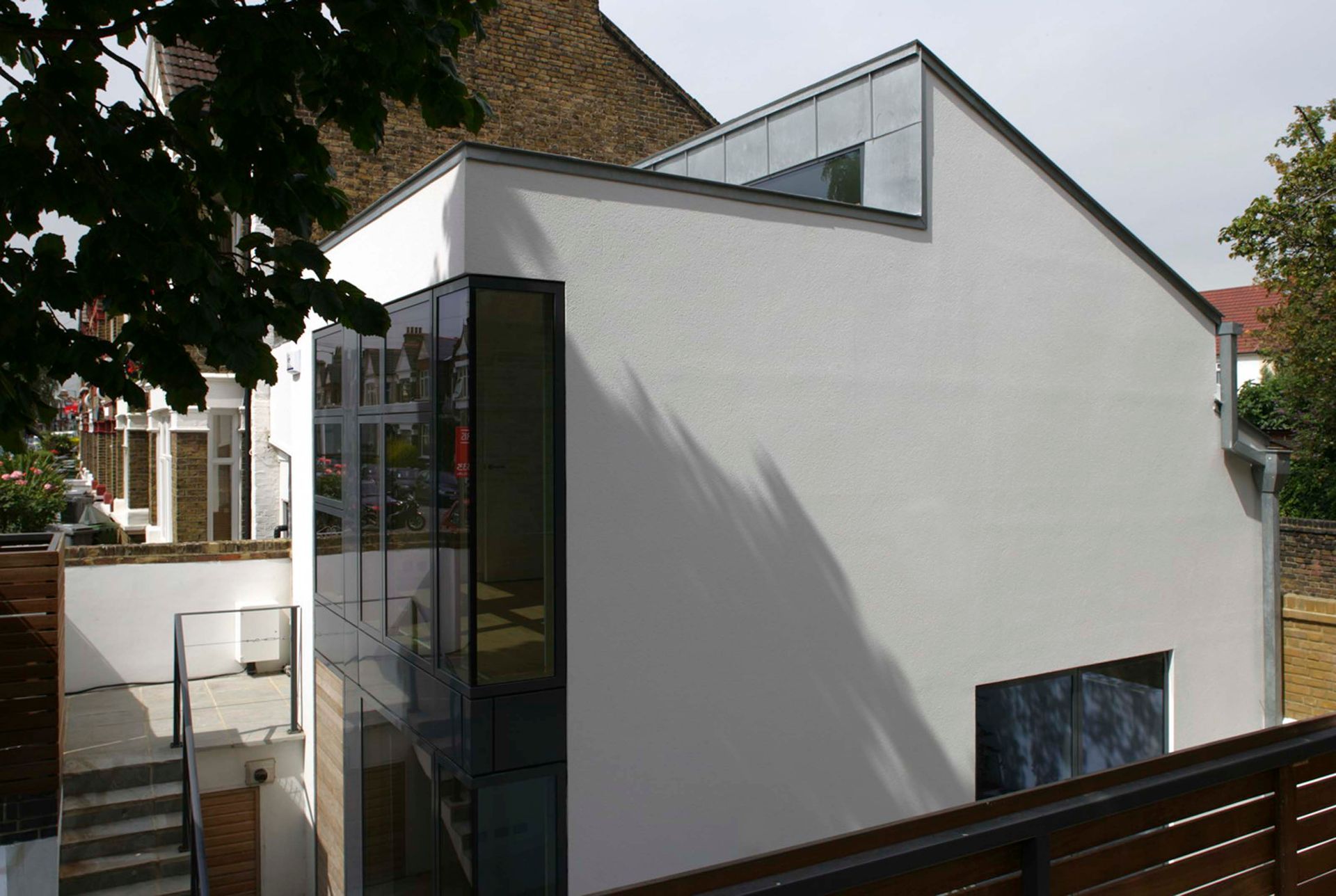 Modern white house with angular roof and large windows, viewed from outside in a leafy neighborhood