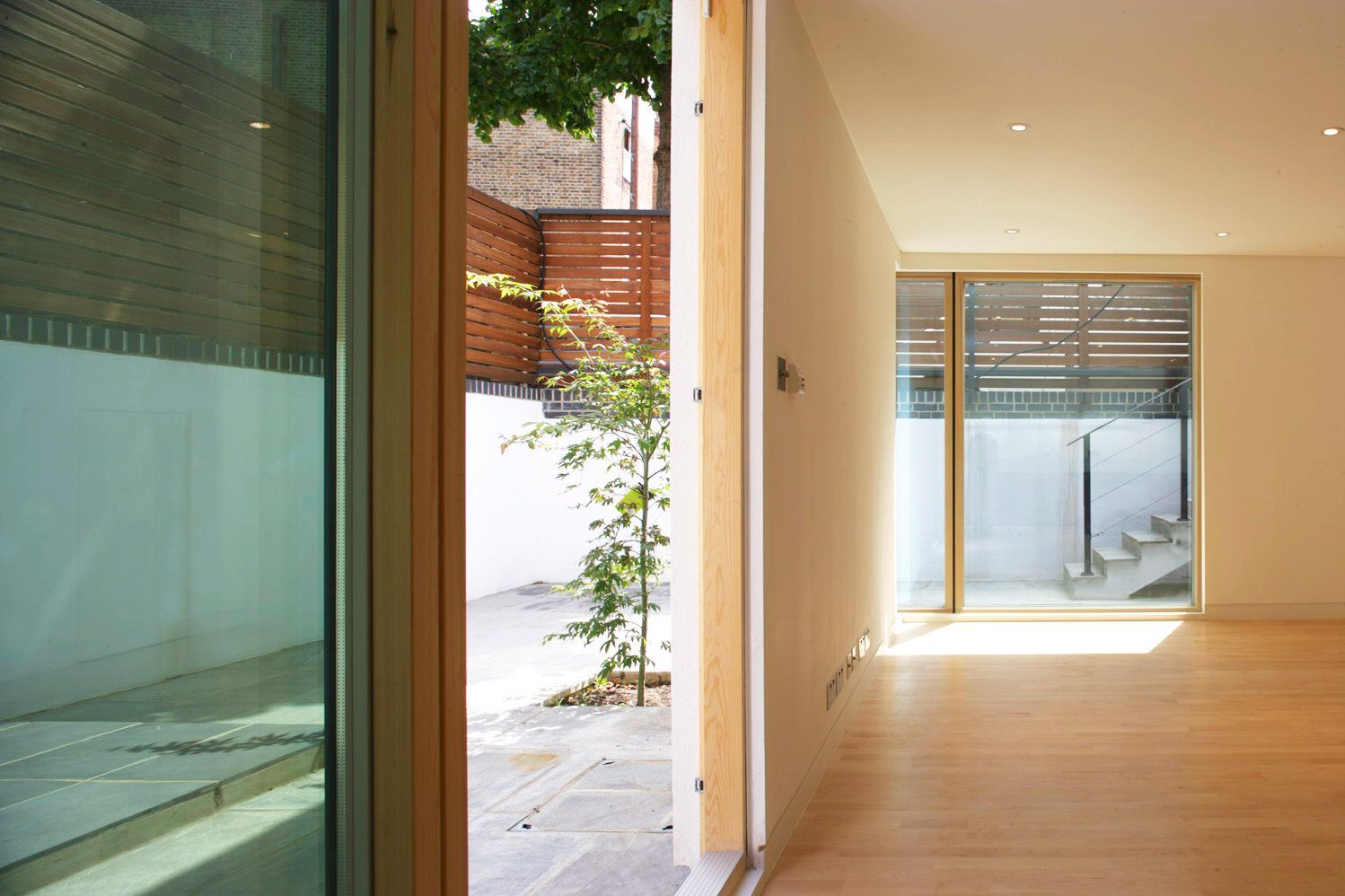 Modern hallway with wood floor, cream walls, and large windows opening to a bright courtyard.