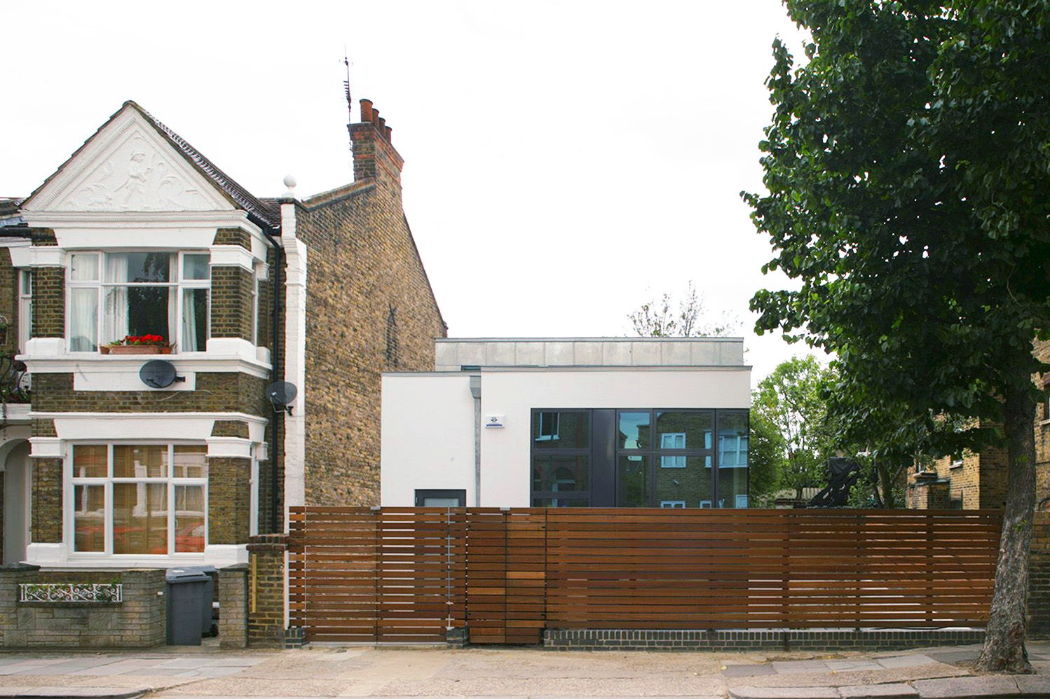 Traditional house beside a modern white building behind a wooden fence and trees