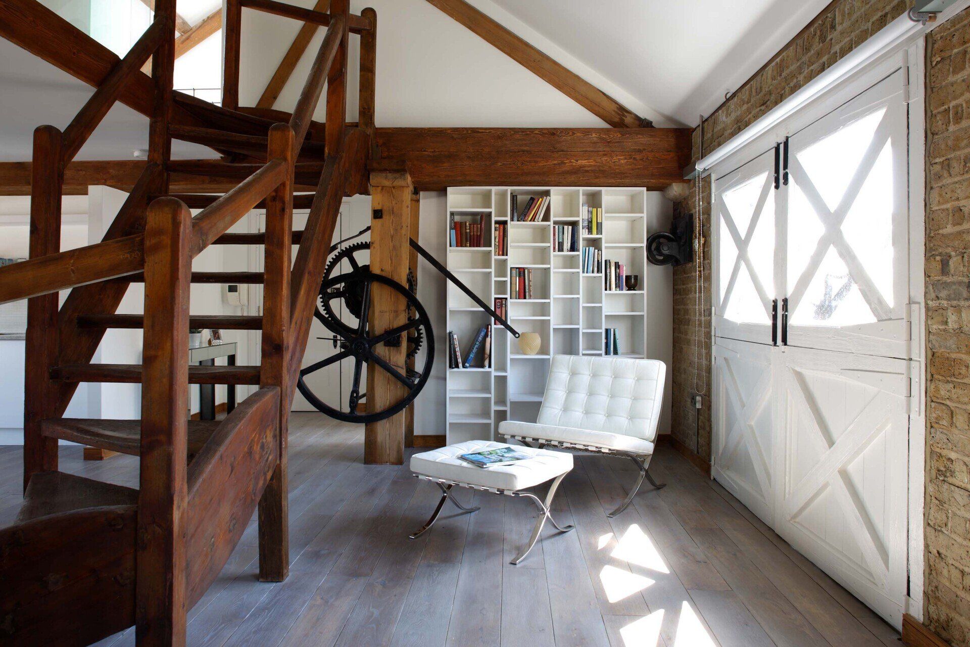 Loft interior with wooden stairs, white chair, and sunlit white door in a rustic room