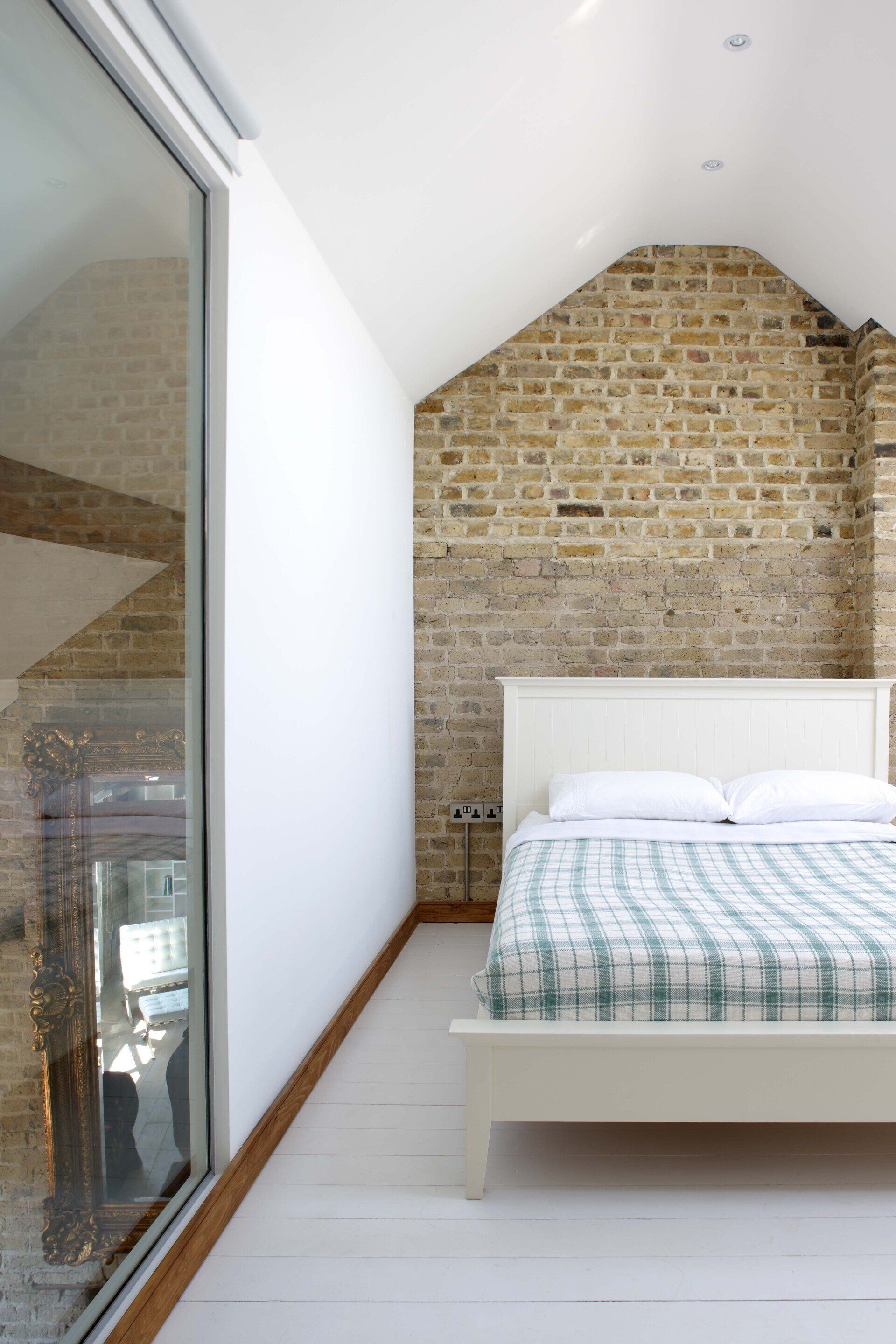 Bright bedroom with exposed brick accent wall, white bed, and large window beside a sloped ceiling