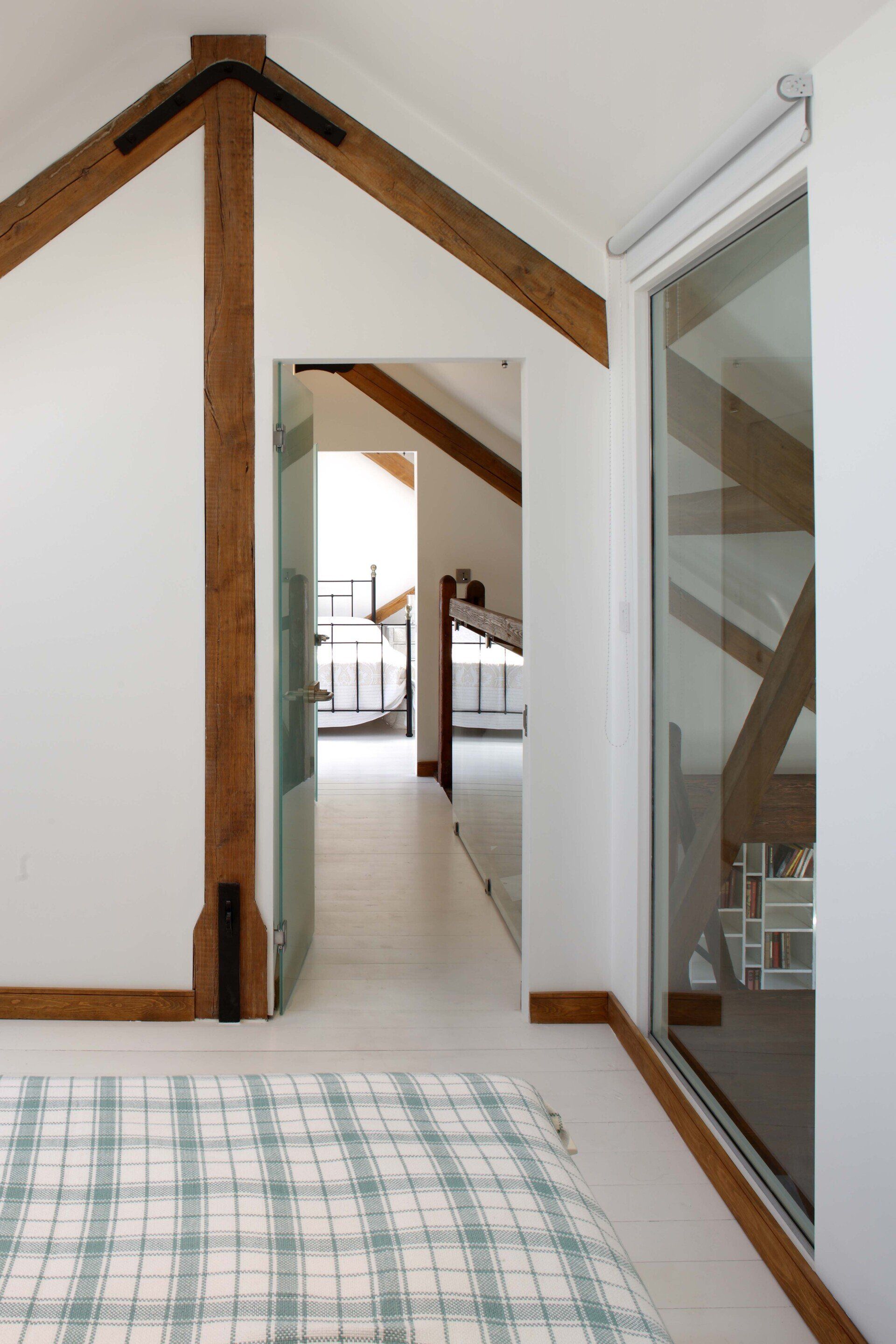 Bedroom loft with white walls, exposed wood beams, and a doorway to a hallway and railing beyond