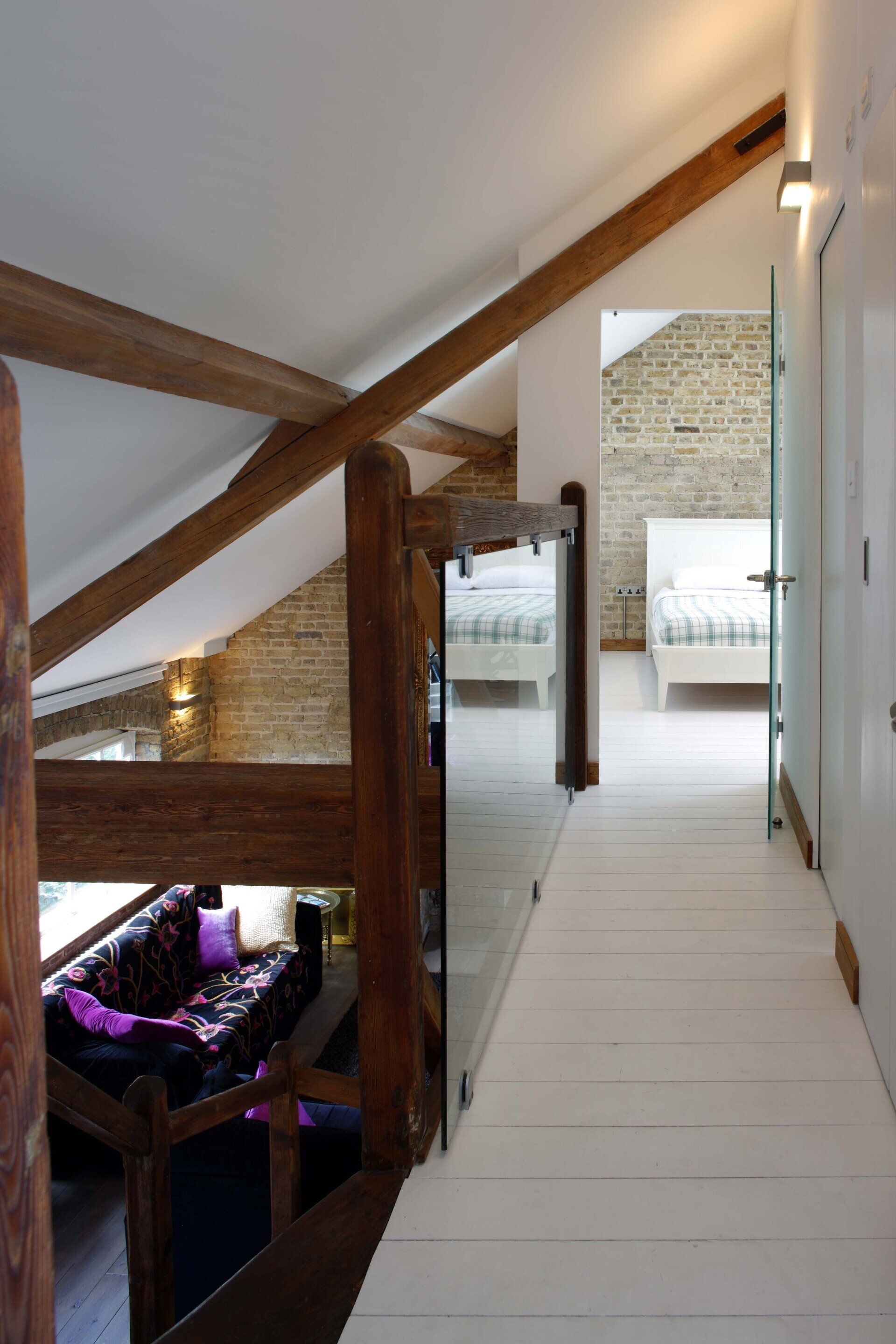 Bright loft hallway with white walls, exposed wood beams, and a view into a cozy room below