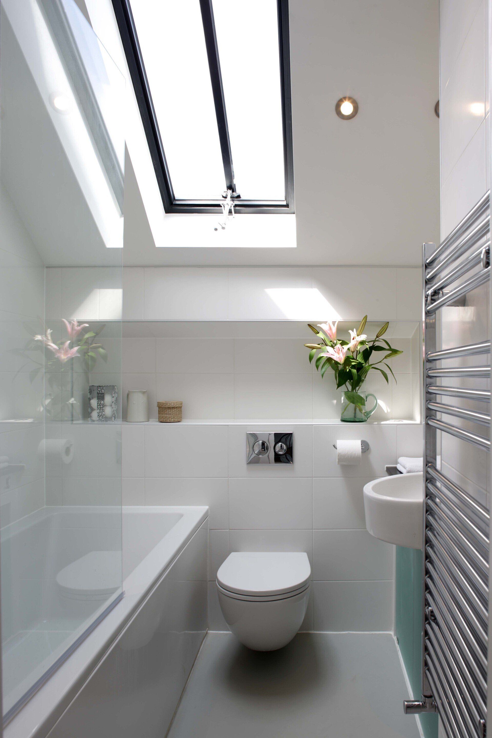 Bright white bathroom with skylight, bathtub, toilet, sink, towel radiator, and flowers