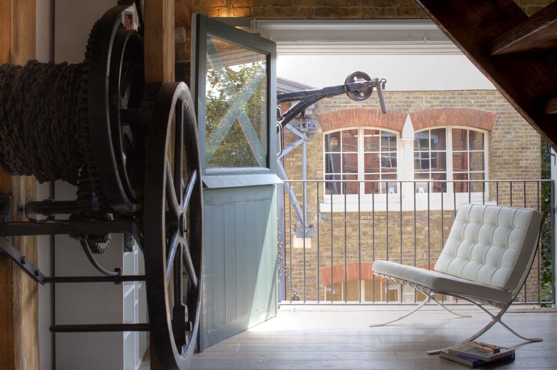 Balcony view through open door with a white chair, metal railing, and brick building across the way