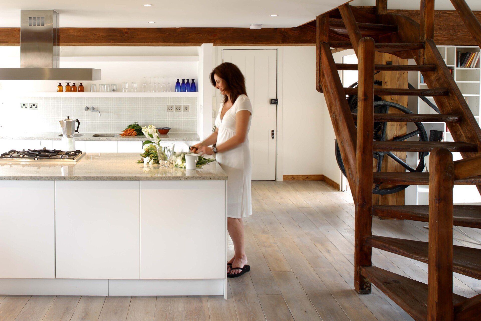 Modern kitchen with white island, wood beams, and a person preparing food near the counter