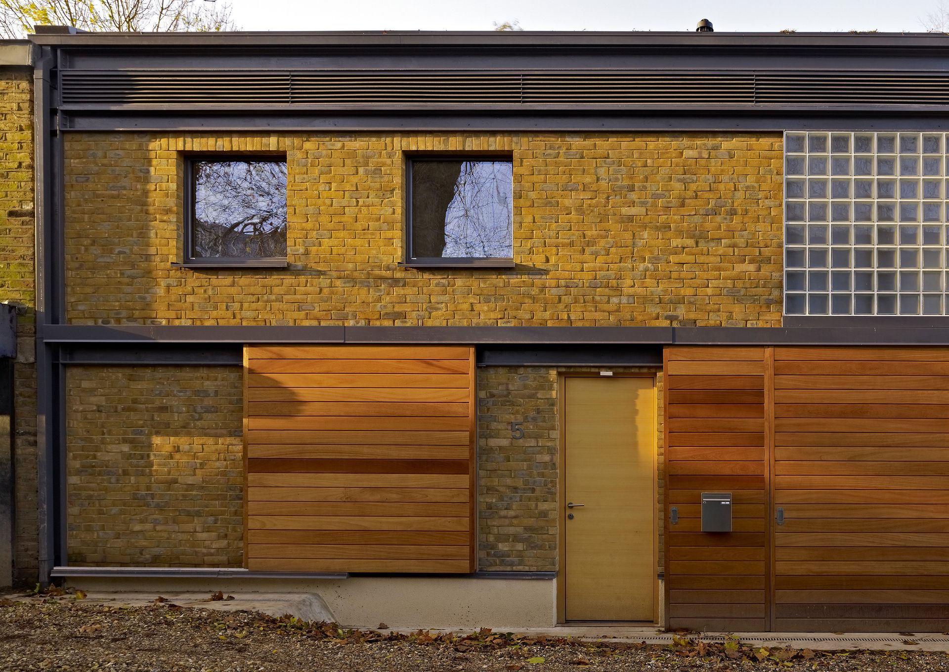 Modern house facade with yellow brick, wooden panels, and a tan door under dark metal trim