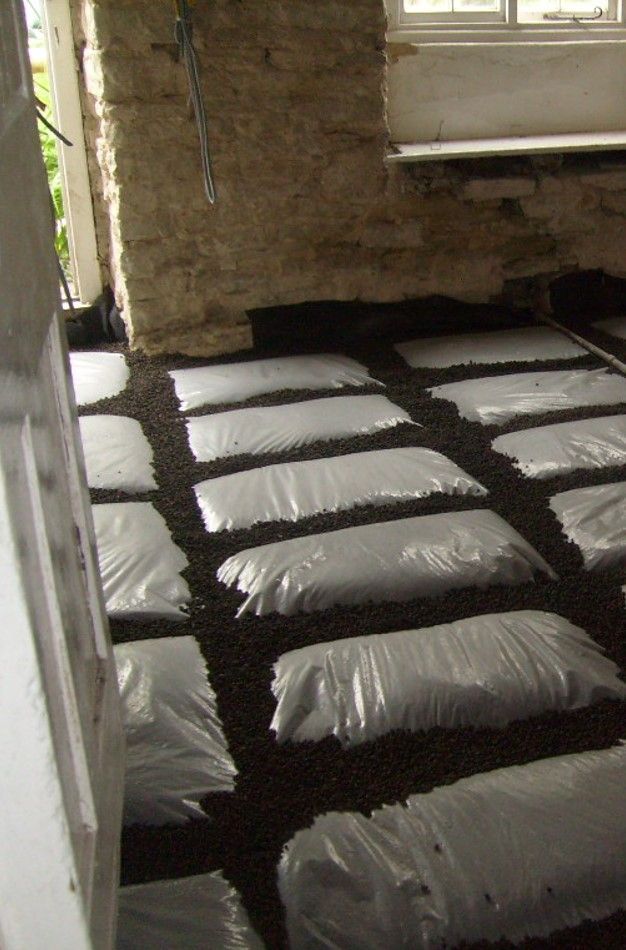 Bags arranged on the floor of a stone room under a window, possibly for insulation or storage.