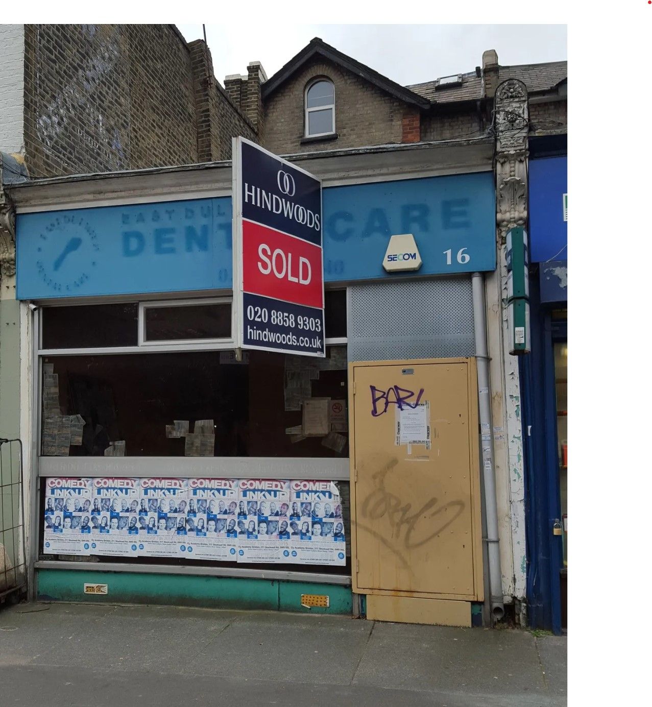 Closed storefront with faded blue signage, a red “SOLD” sign, and a boarded doorway on a city street
