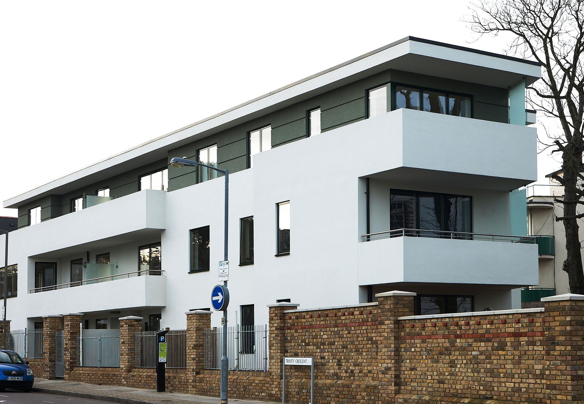 Modern white apartment building with balconies behind a brick wall on a street corner