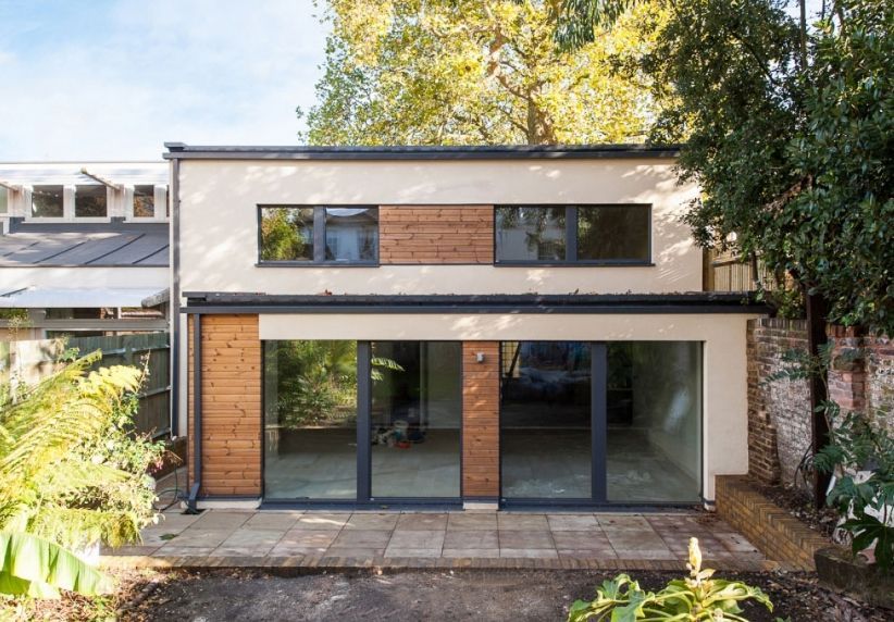 Modern two-story house with large glass doors, wood accents, and a leafy front garden