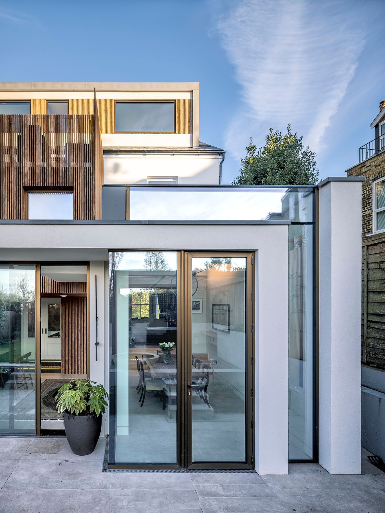 Modern house exterior with large glass doors, white and wood facade, and a potted plant by the entrance