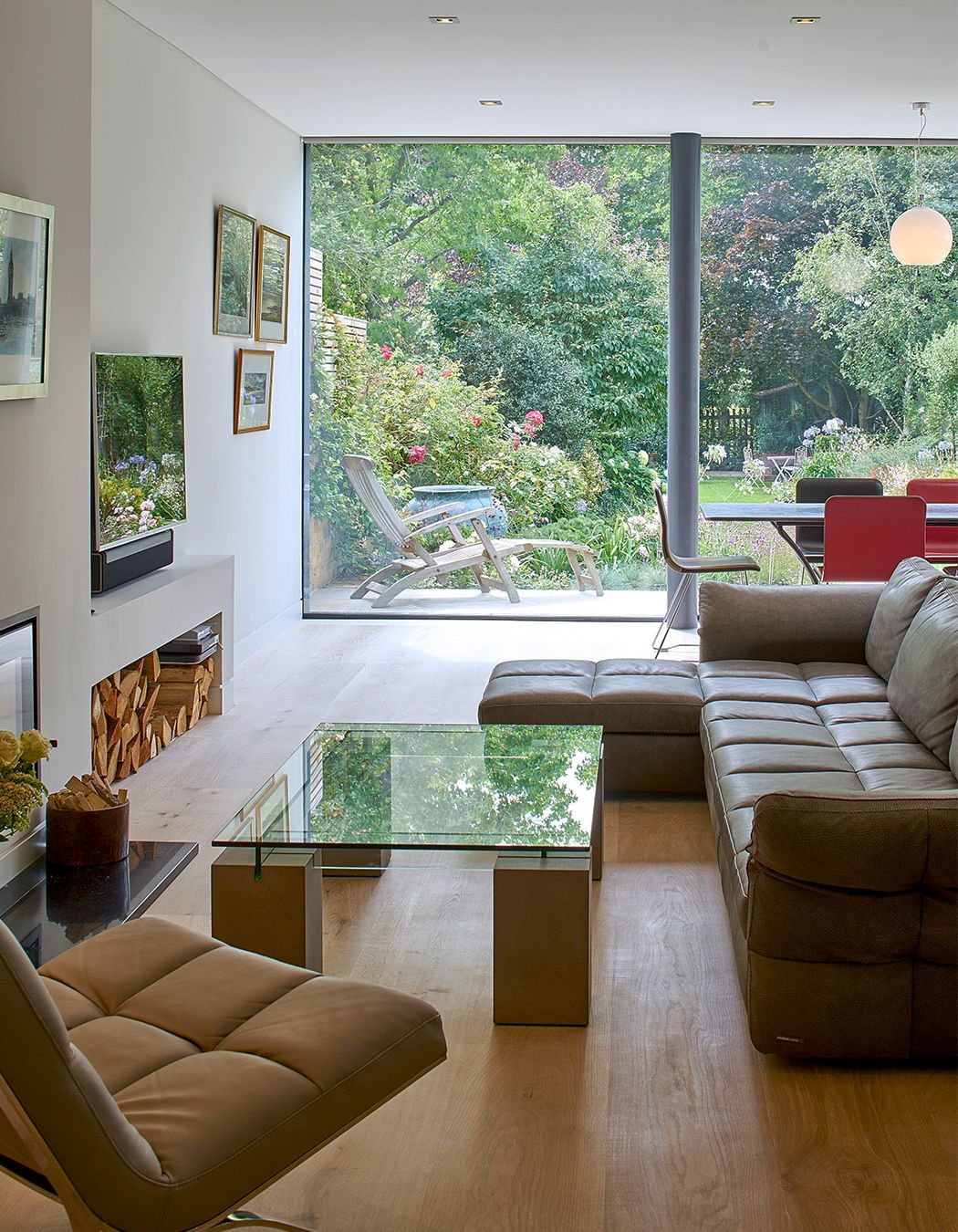 Modern living room with beige sofa, glass coffee table, fireplace, and large garden-view windows