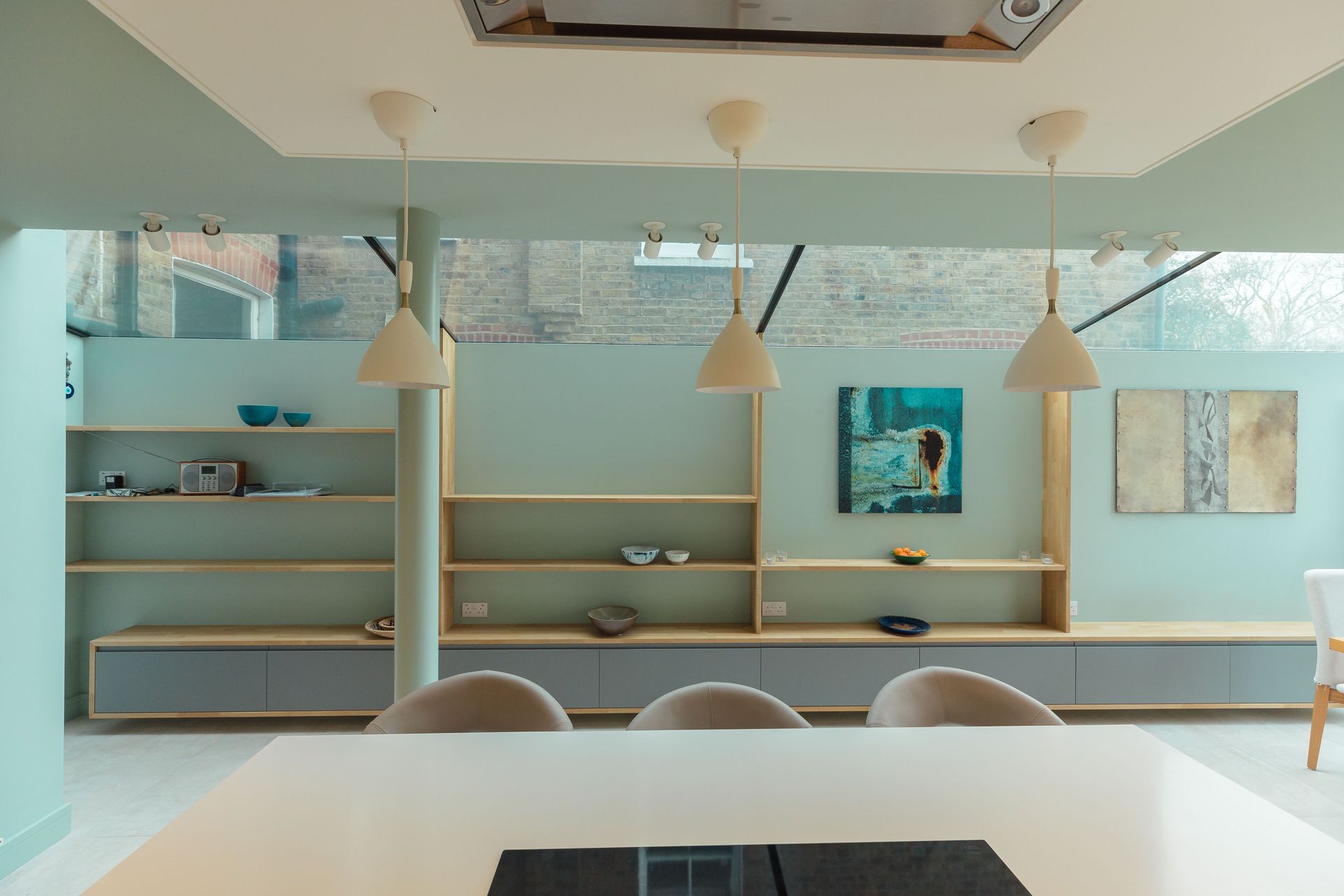 Minimalist café interior with pale blue walls, wooden shelves, pendant lights, and white tables and chairs