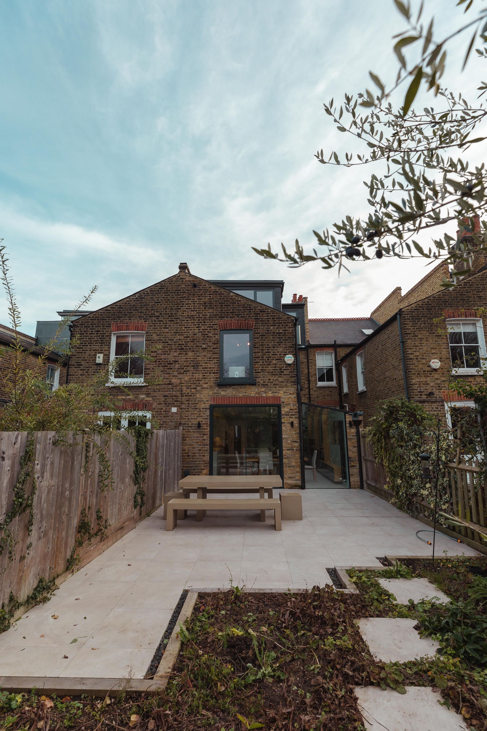 Brick backyard patio with bench, surrounding fences, and a brick house under a pale blue sky