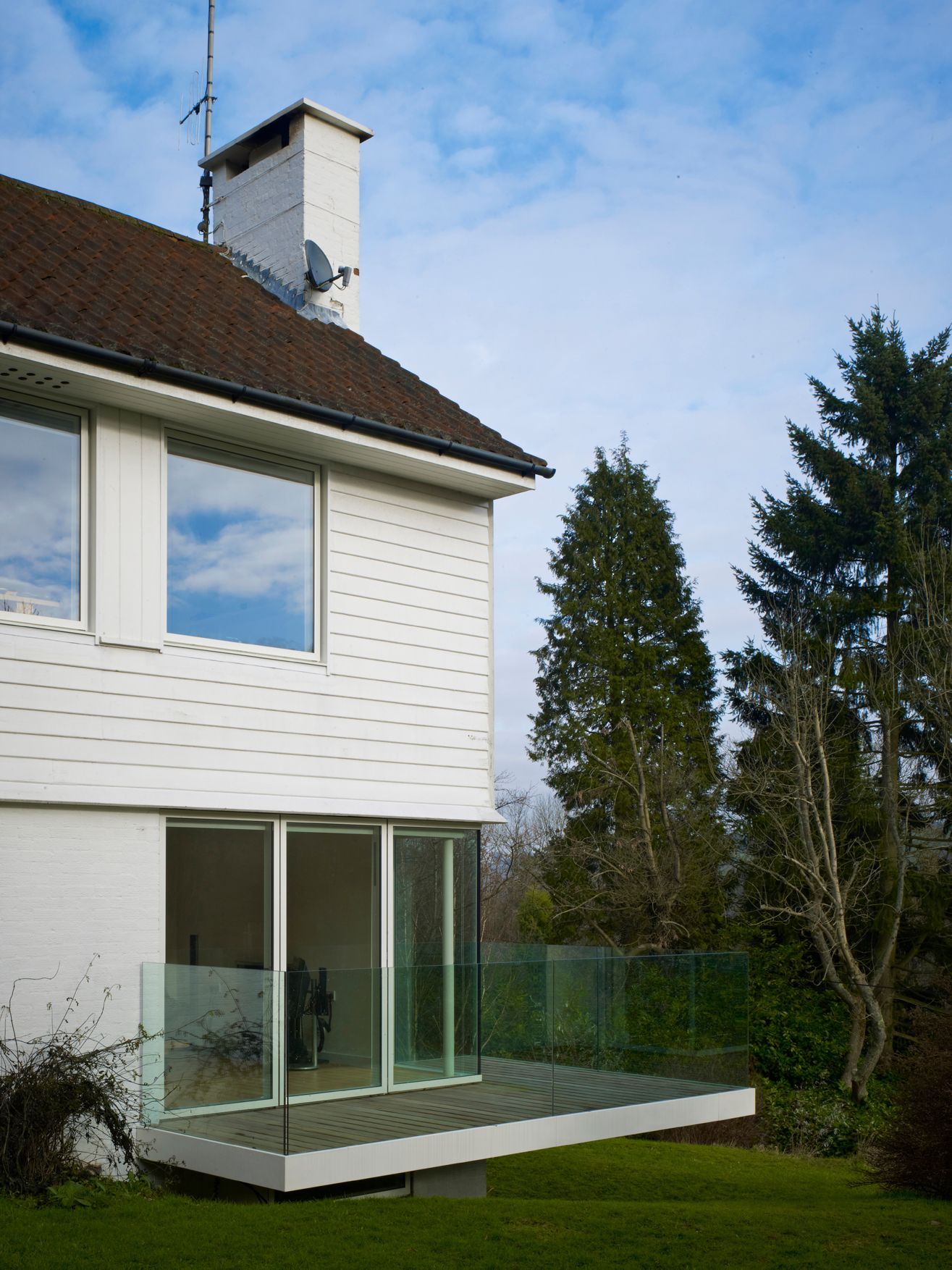 White house exterior with a small balcony and large glass doors overlooking a green backyard