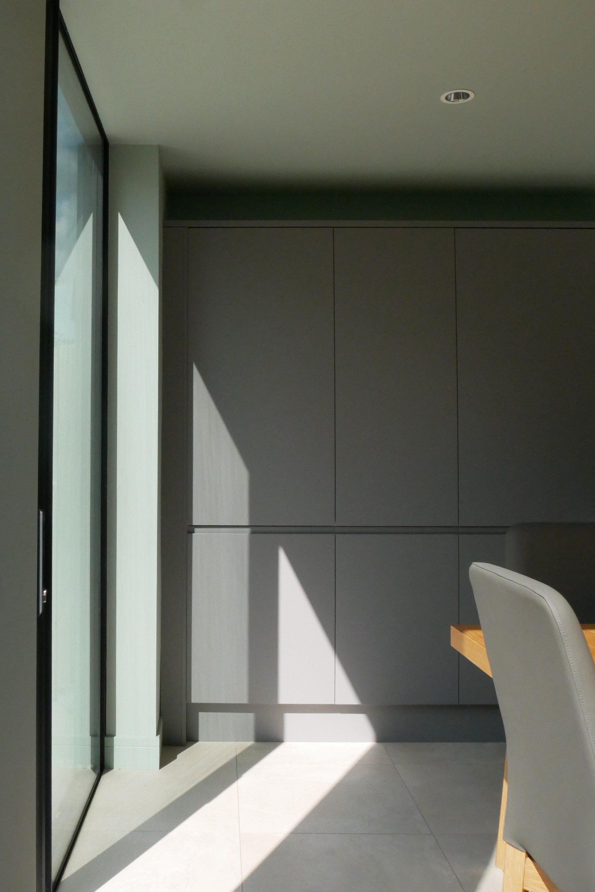 Bright balcony with glass doors, gray wall, and a white chair in sunlight