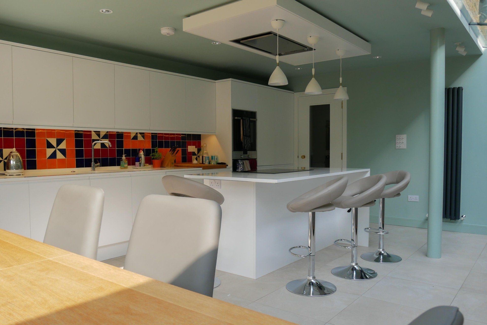 Modern kitchen with white island, bar stools, pendant lights, and colorful backsplash