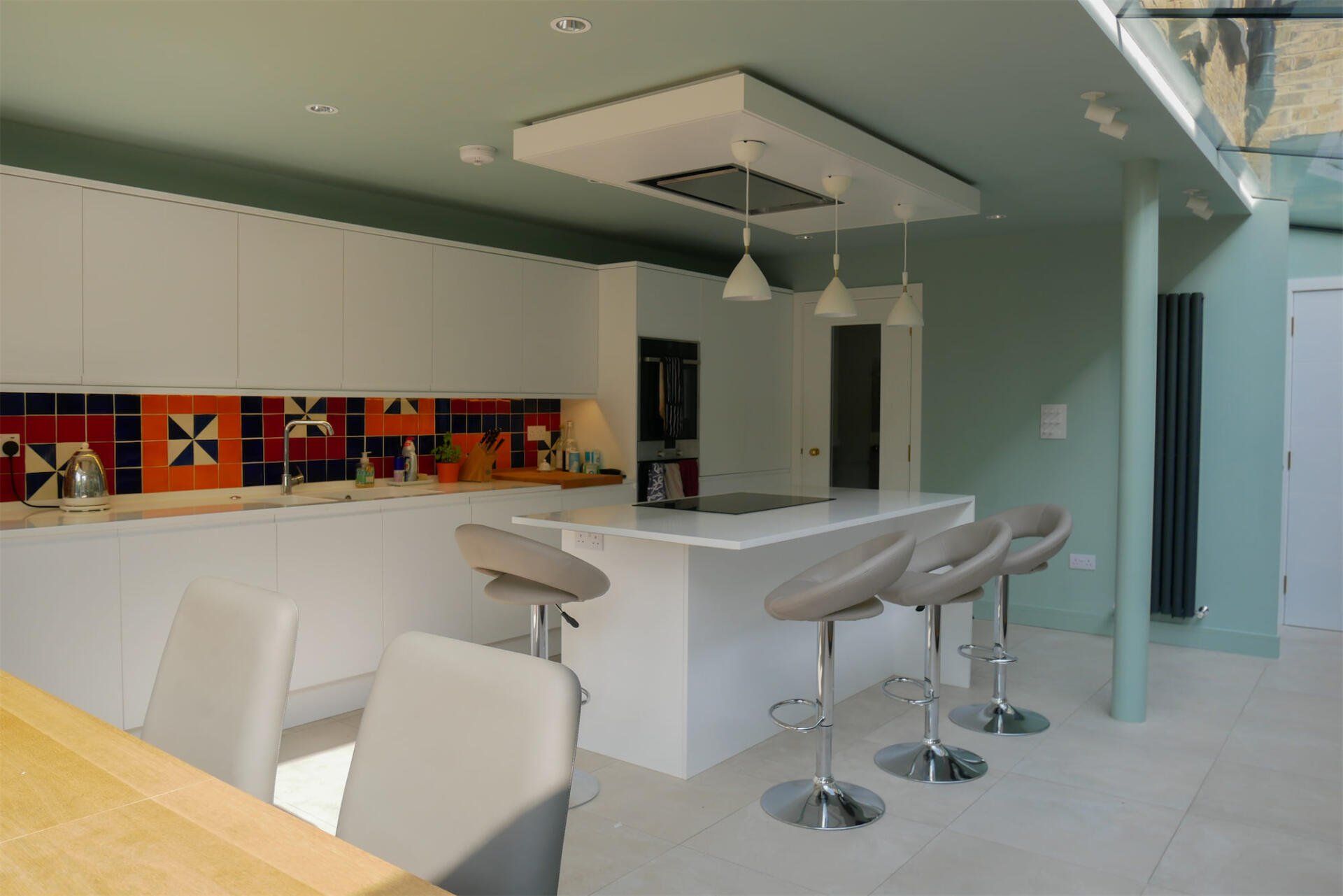 Modern kitchen with white island, bar stools, mosaic backsplash, and light teal walls