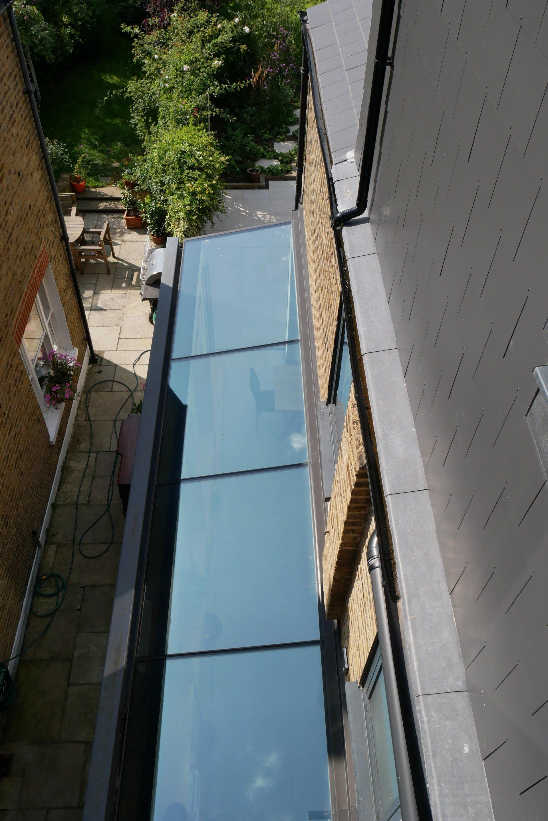 Narrow outdoor passage with a light blue translucent roof between buildings and greenery.