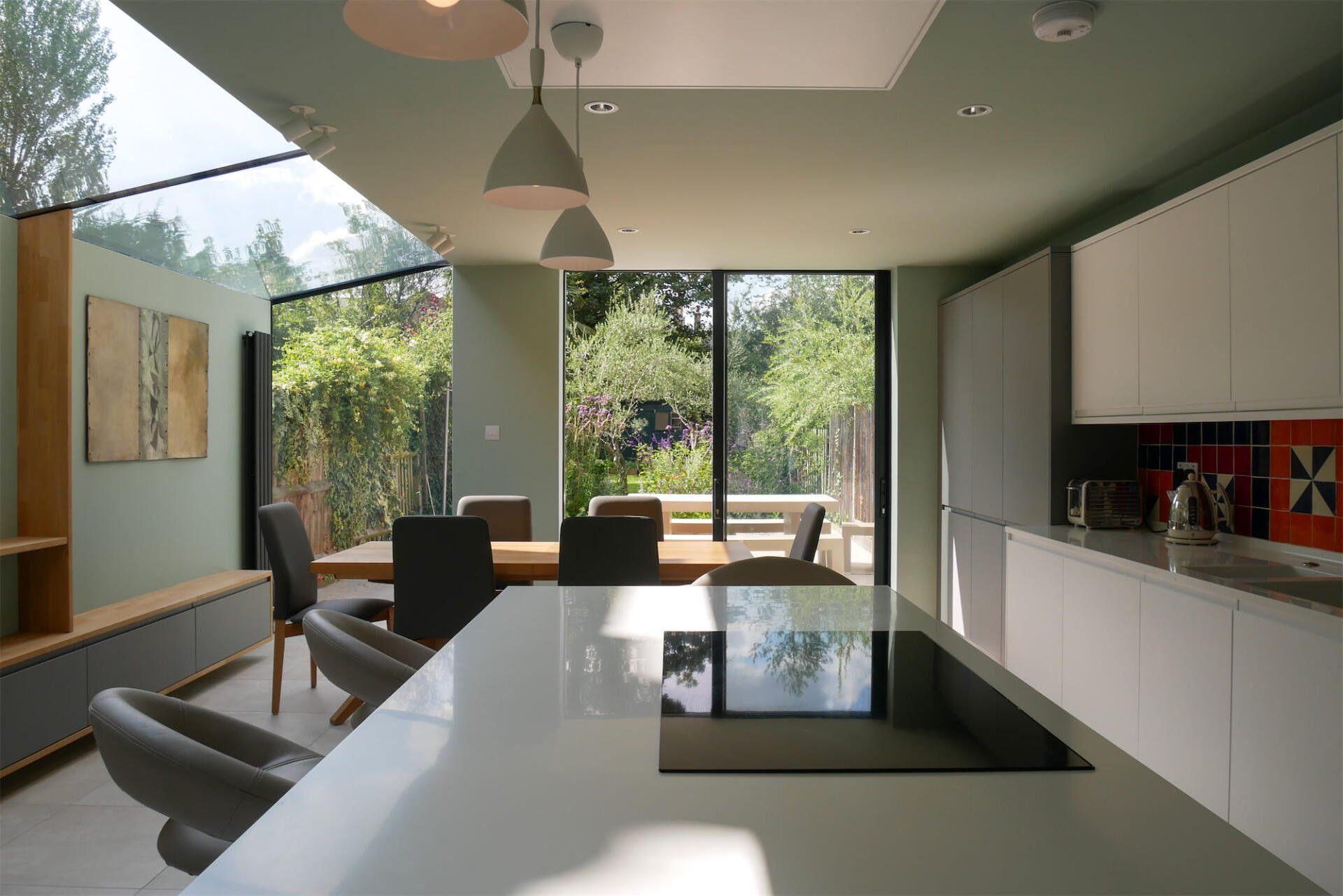 Modern kitchen-dining area with white cabinets, island, and large windows overlooking greenery