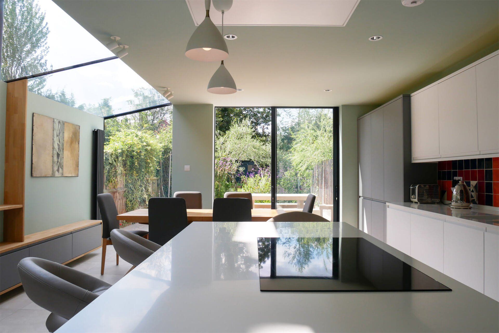 Modern kitchen with white cabinets, glossy island, pendant lights, and large glass doors opening to a green yard