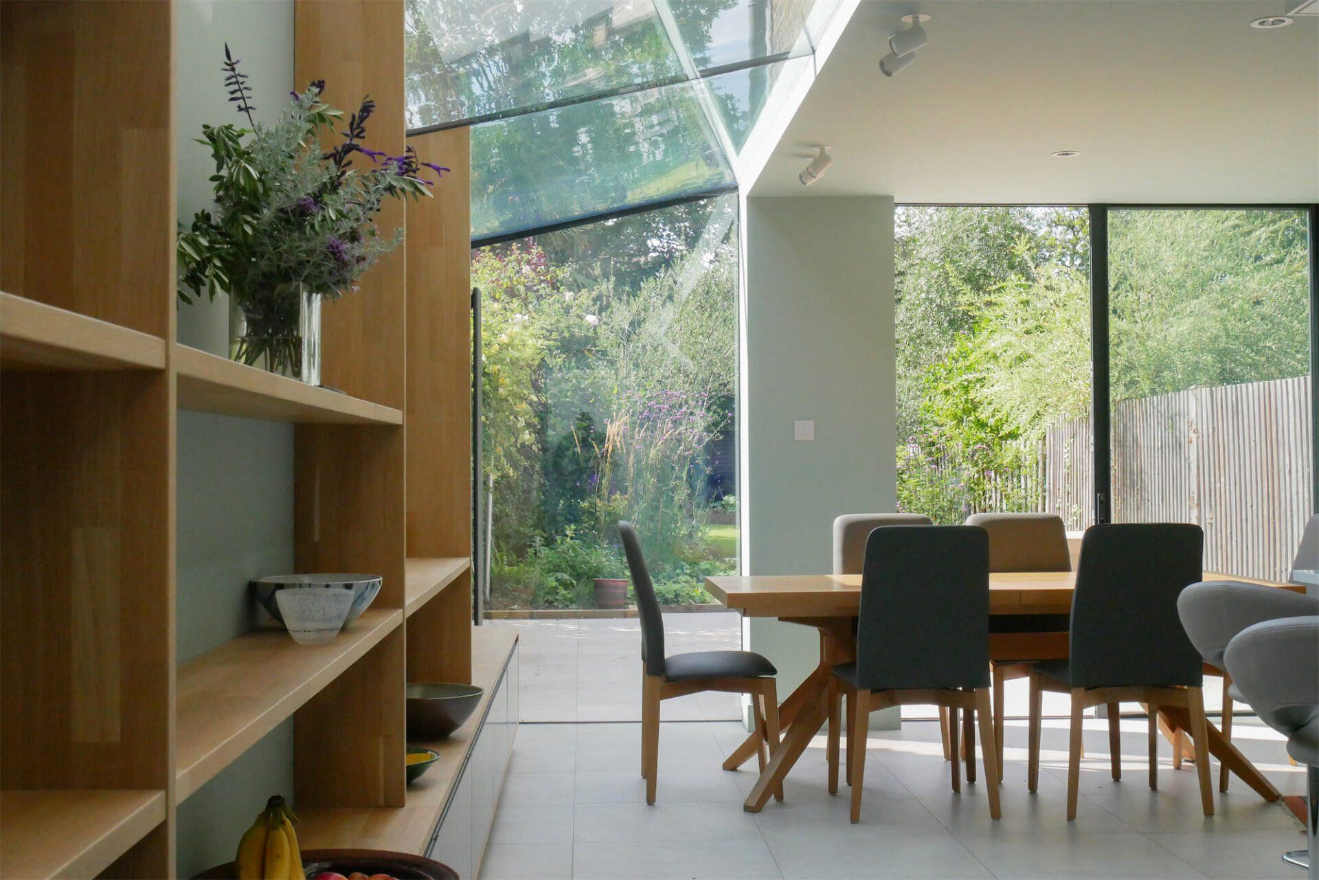 Modern dining room with large windows, wooden table, and chairs overlooking a green garden.