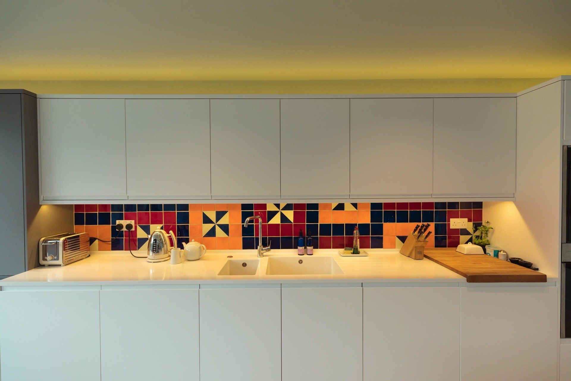 Modern kitchen with white cabinets, colorful tile backsplash, and wooden countertop with dishes and utensils