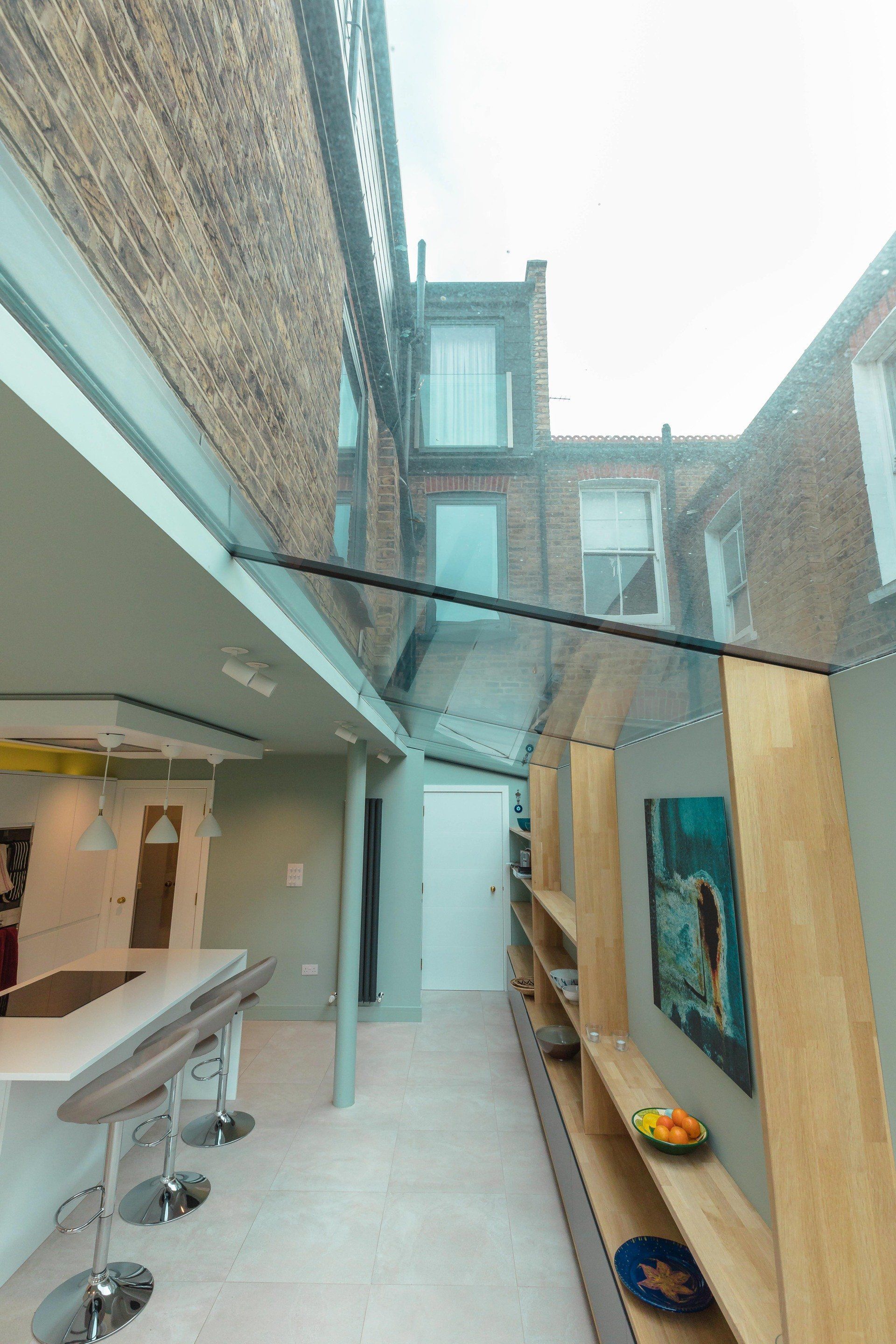 Narrow outdoor courtyard with brick walls, skylight, and a small dining area with stools and wall art.