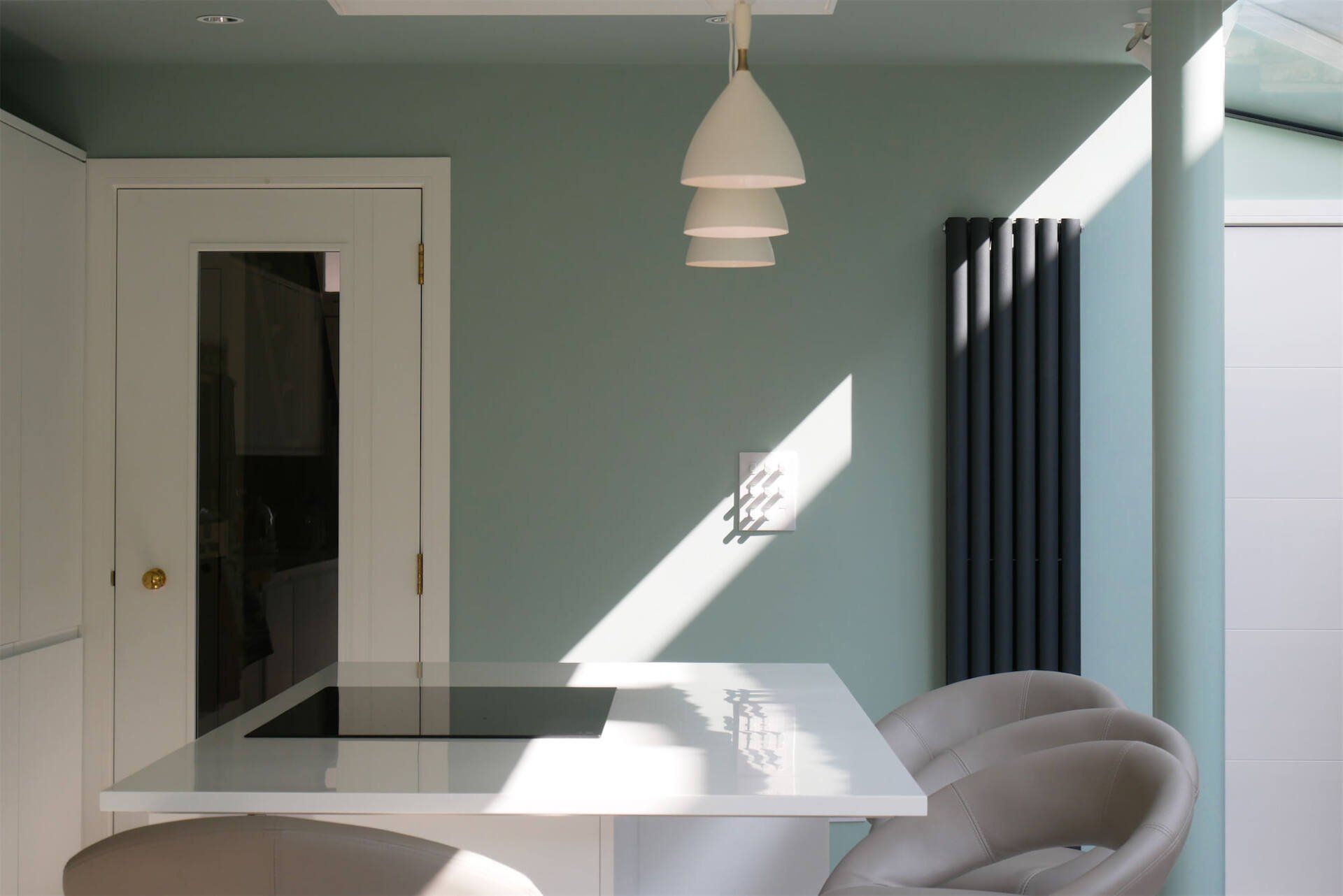 Bright dining room with mint walls, white table and chairs, pendant light, and sunlight casting sharp shadows.