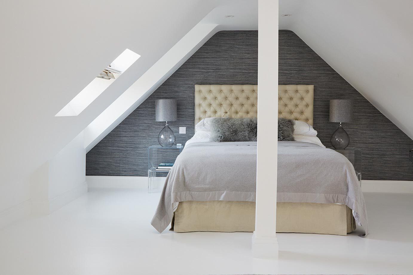 Loft bedroom with a bed beneath sloped ceiling, dark accent wall, and skylight windows.