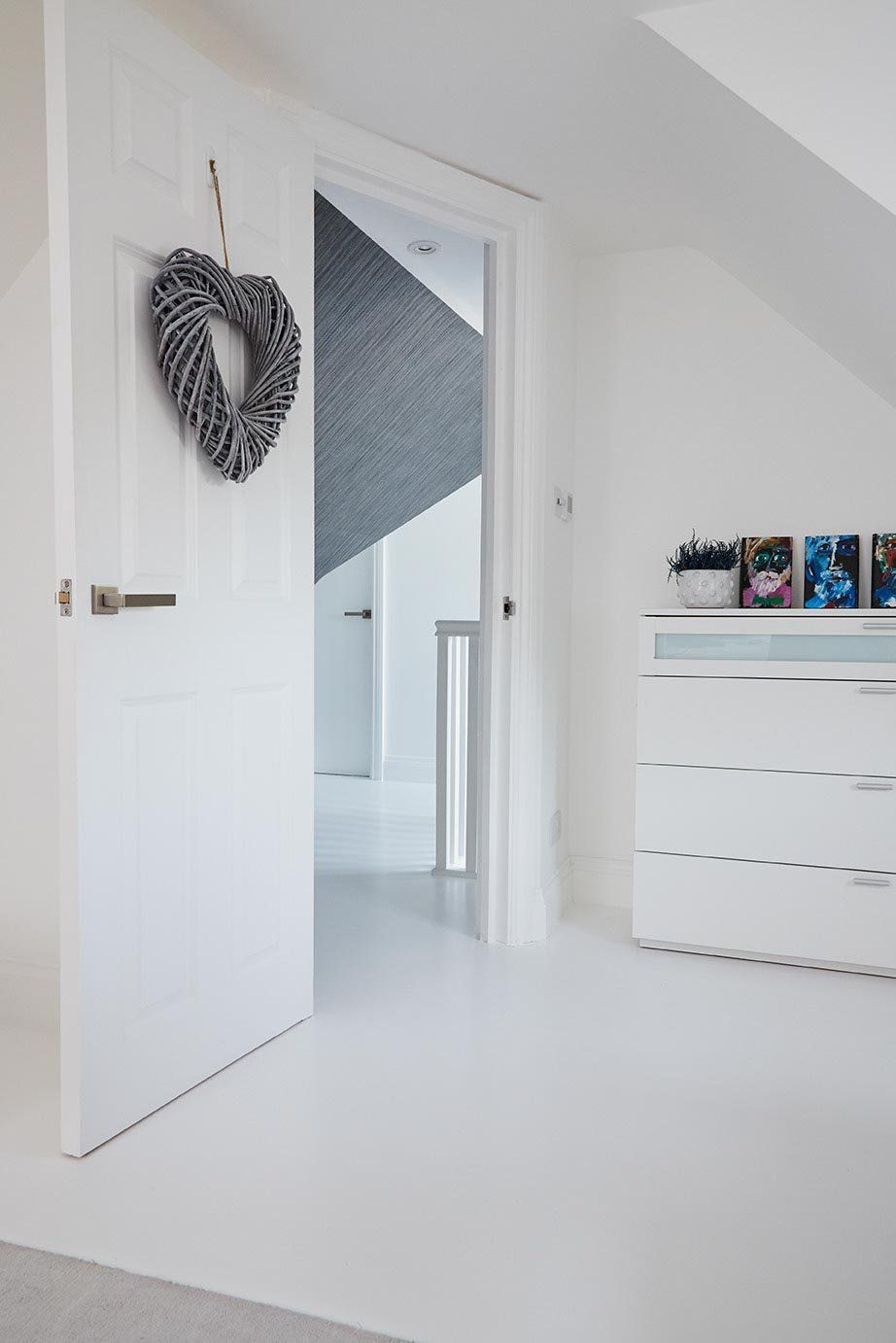 White hallway with open door, heart wreath, and dresser in a bright minimalist home