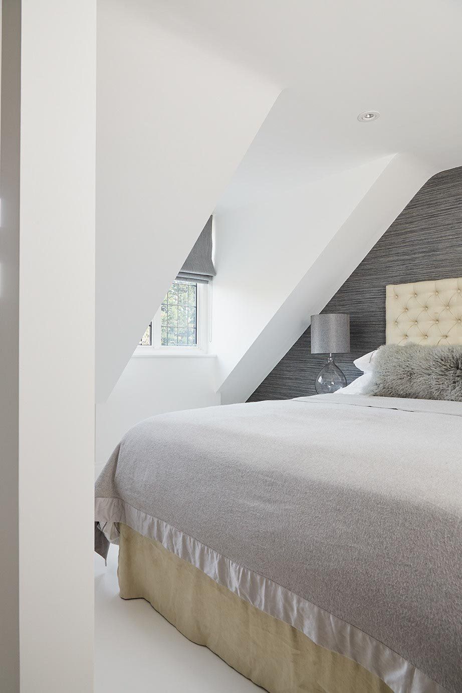 Modern attic bedroom with sloped ceiling, gray bed, and small window
